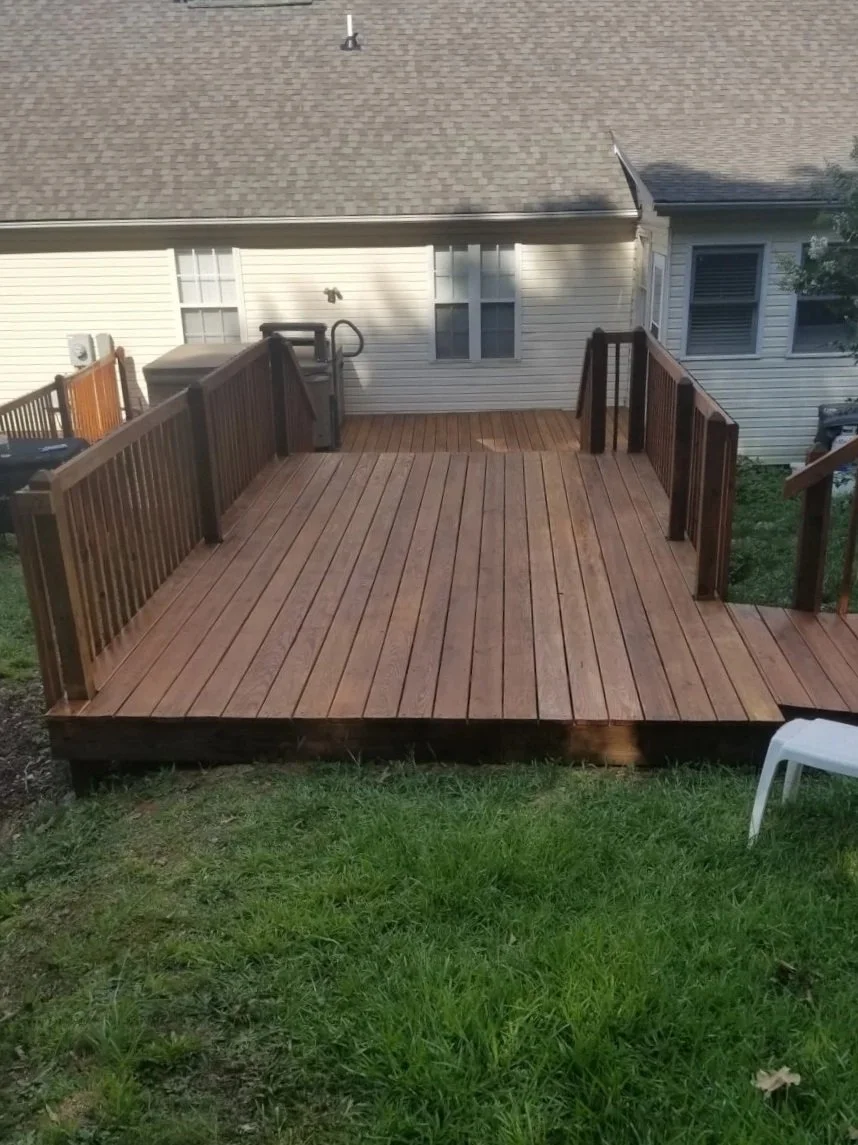 Wooden deck with railings attached to back of house, showing grassy yard and house with white siding in the background.
