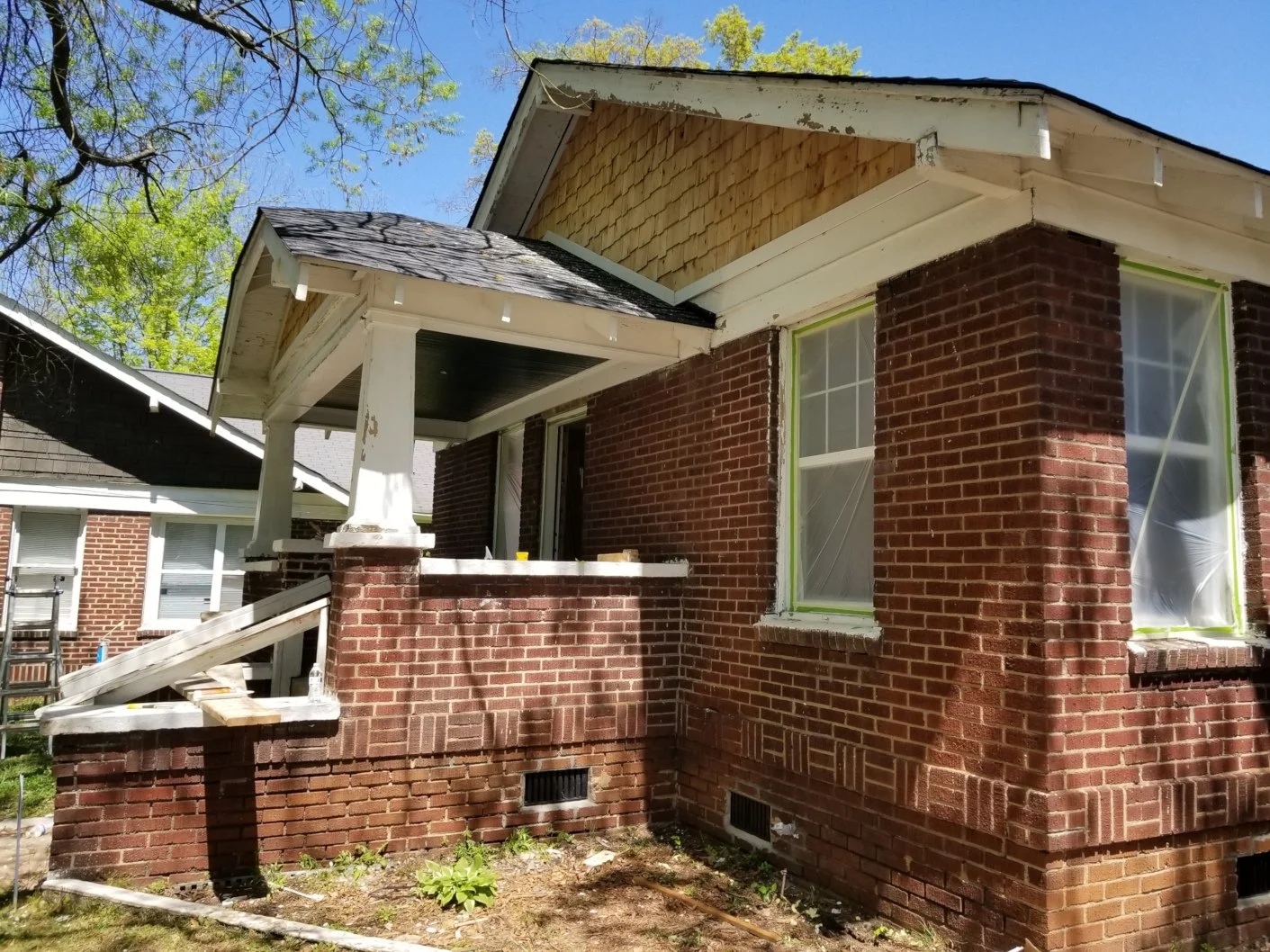 House under renovation with brick exterior, some windows covered with plastic, staircase leading to entrance, and construction materials around.