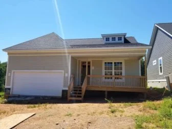 Newly built house with a front porch and stairs, located in a suburban area under a blue sky.