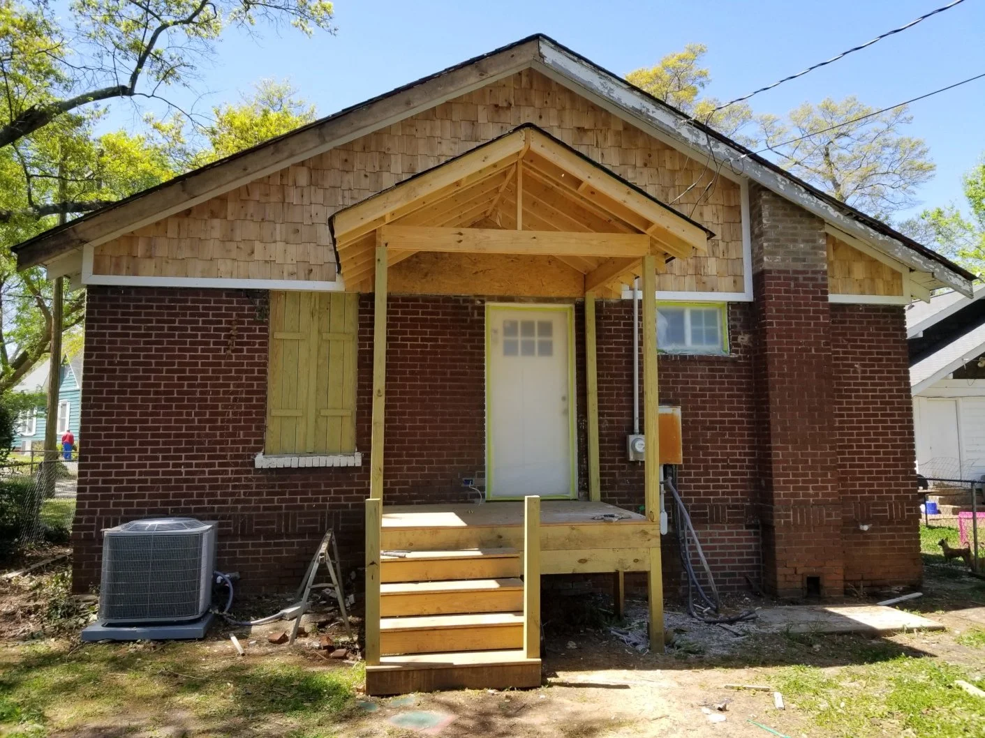 Back of house under construction with new porch and stairs, brick exterior, and open space where a door and window will be installed.