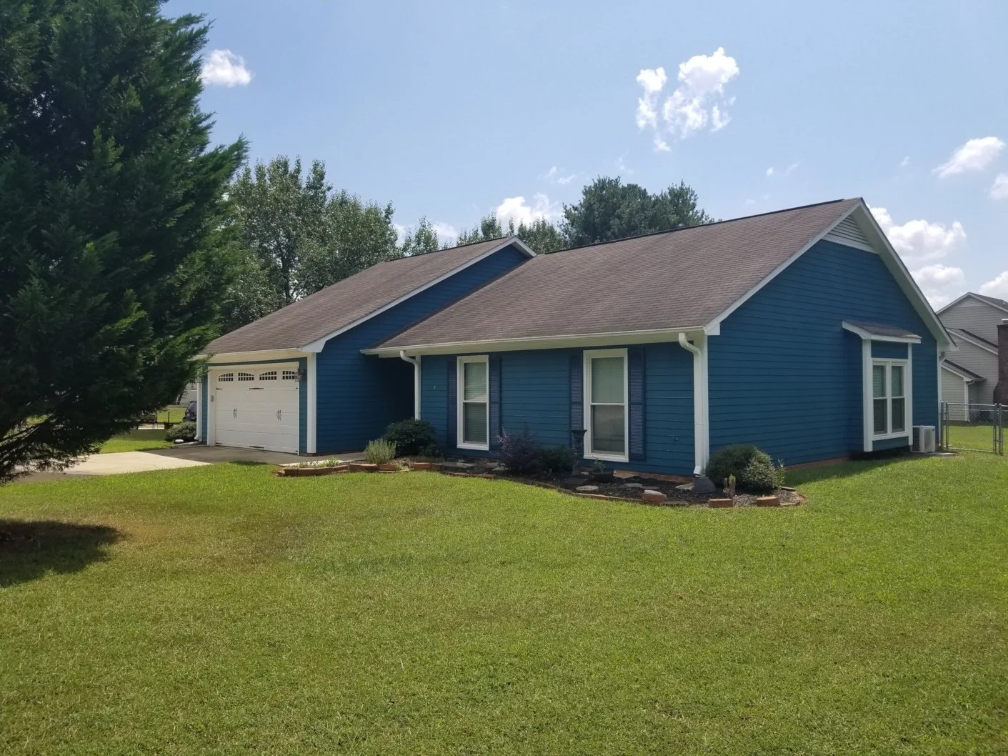 A blue suburban house with a white garage door and a well-maintained lawn under a partly cloudy sky.