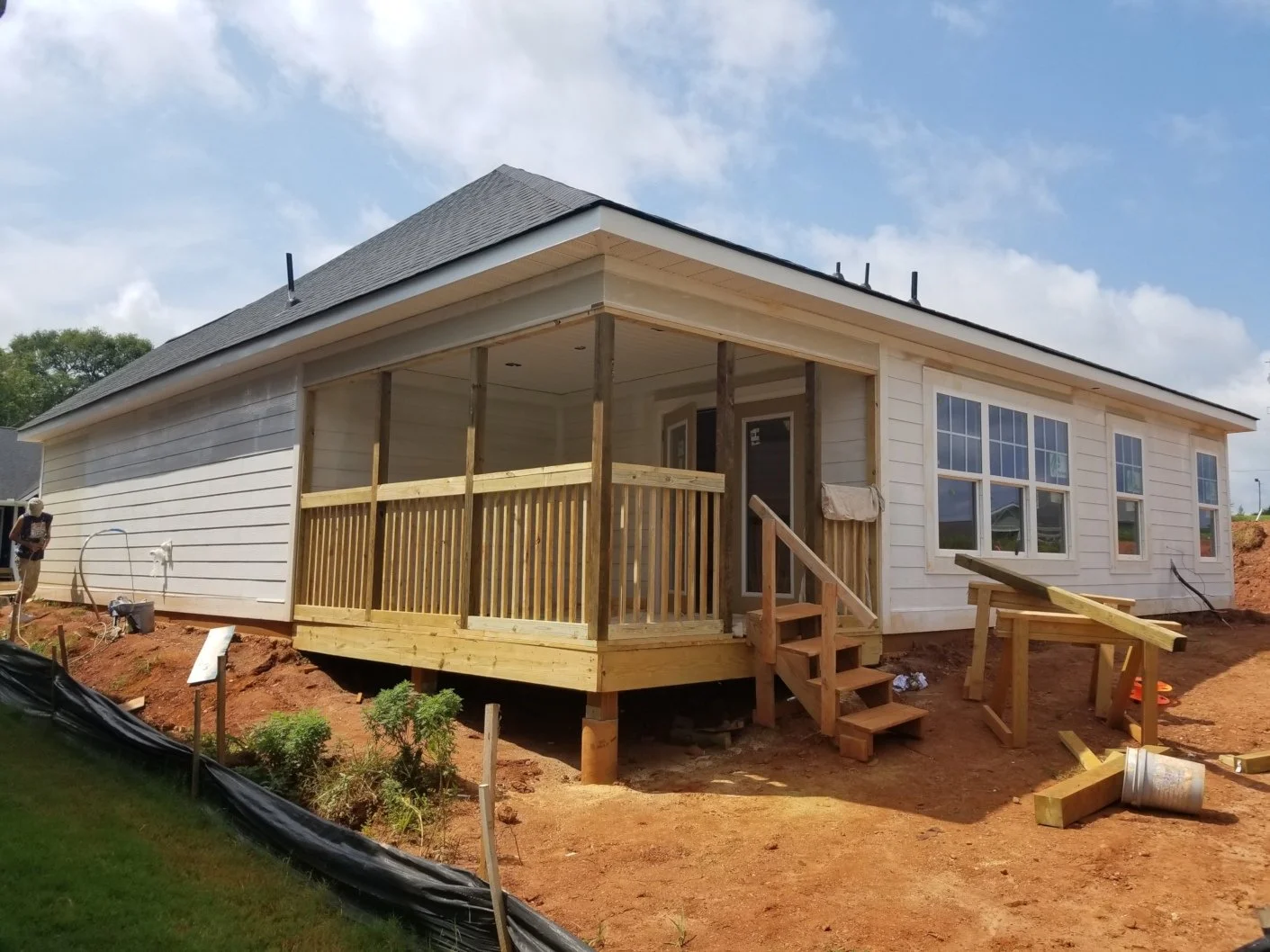 House under construction with a new wooden porch and steps, windows, and a partially finished exterior, on a construction site with dirt and construction materials.