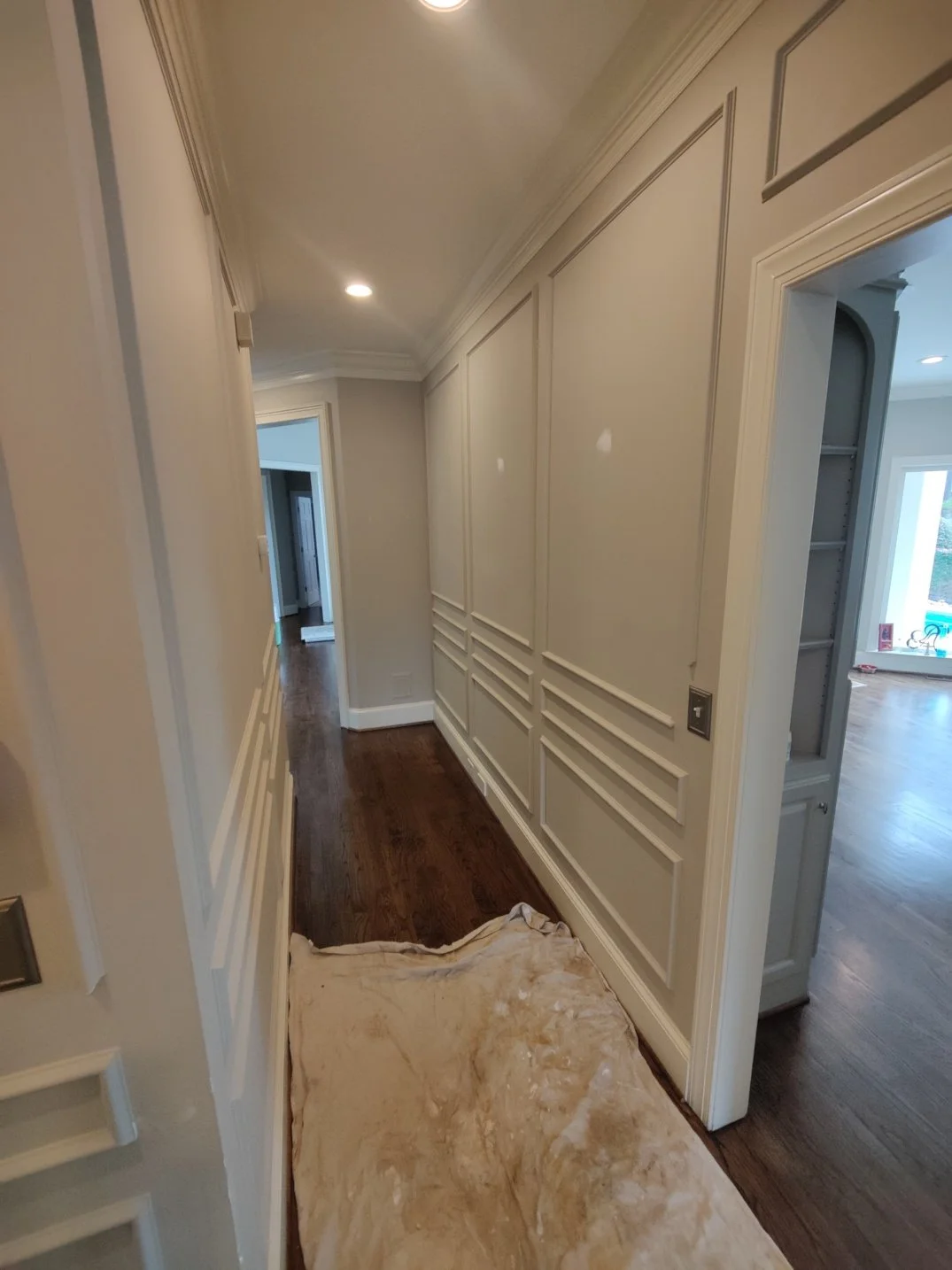 Interior hallway of a house with beige walls, decorative molding, dark hardwood flooring, and a beige cloth on the floor.