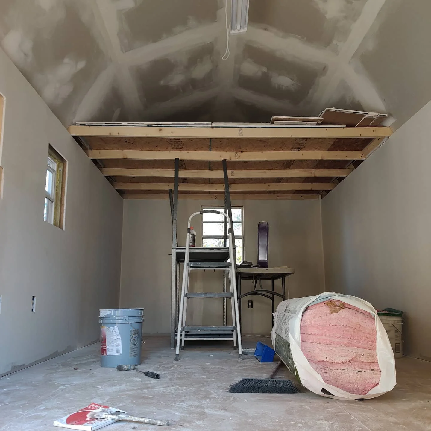 Room under construction with drywall, insulation, ladder, and construction tools.