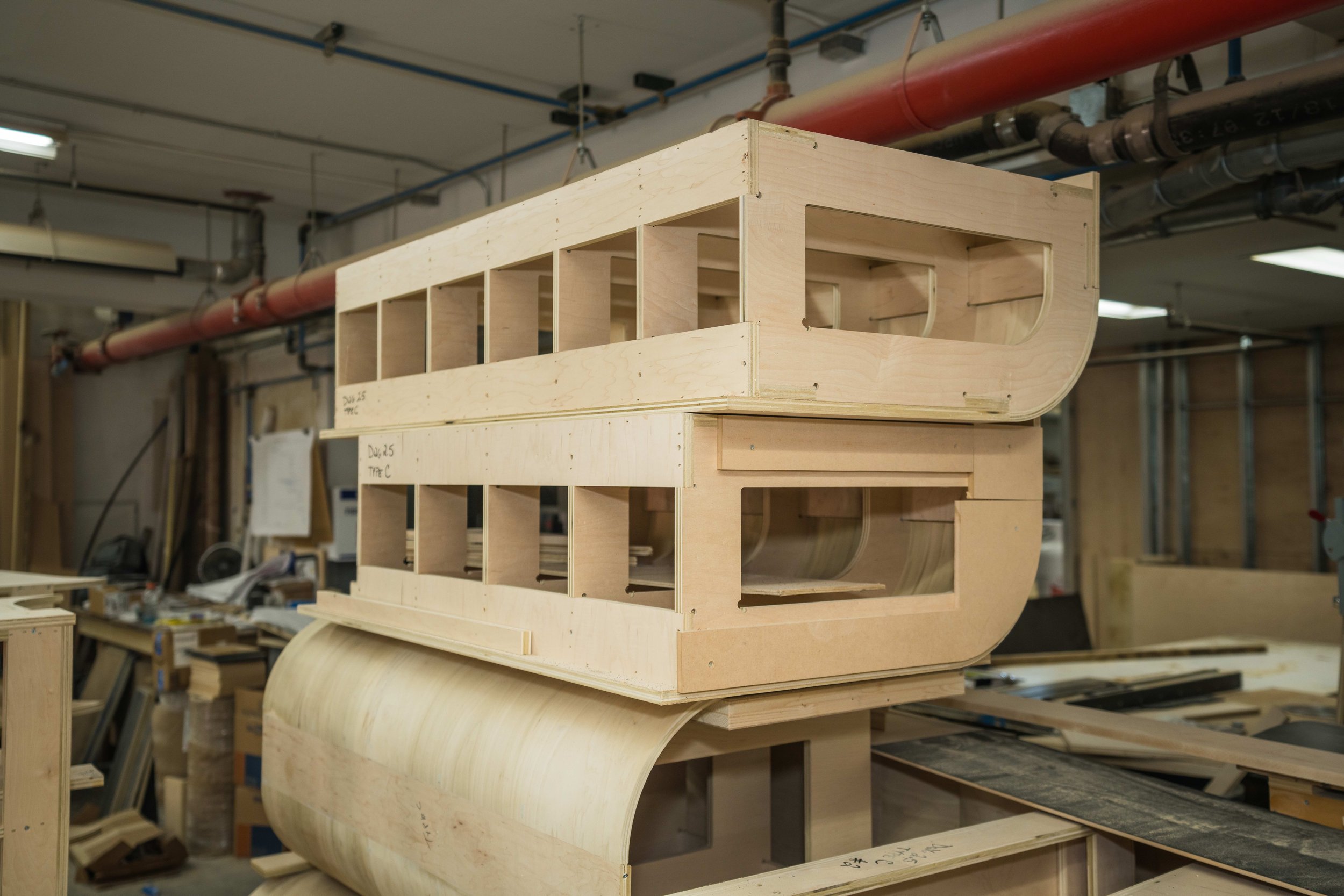Wooden boat hull under construction in a workshop with woodworking tools and materials.
