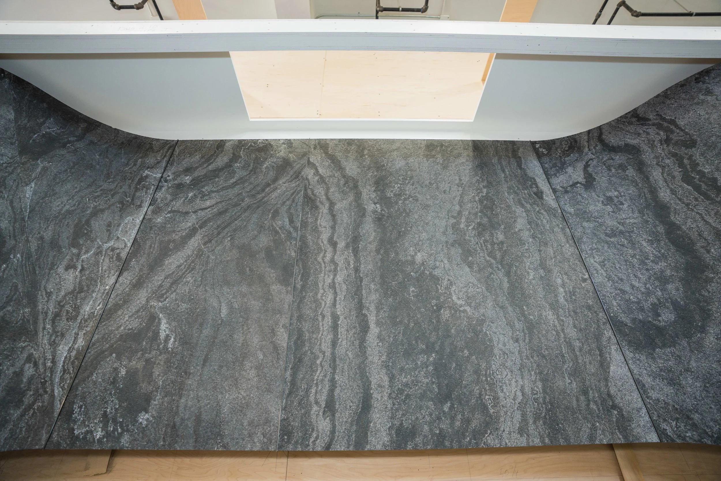 Top view of a section of gray marble flooring with a white raised platform or counter at the top and a light wooden edge at the bottom.