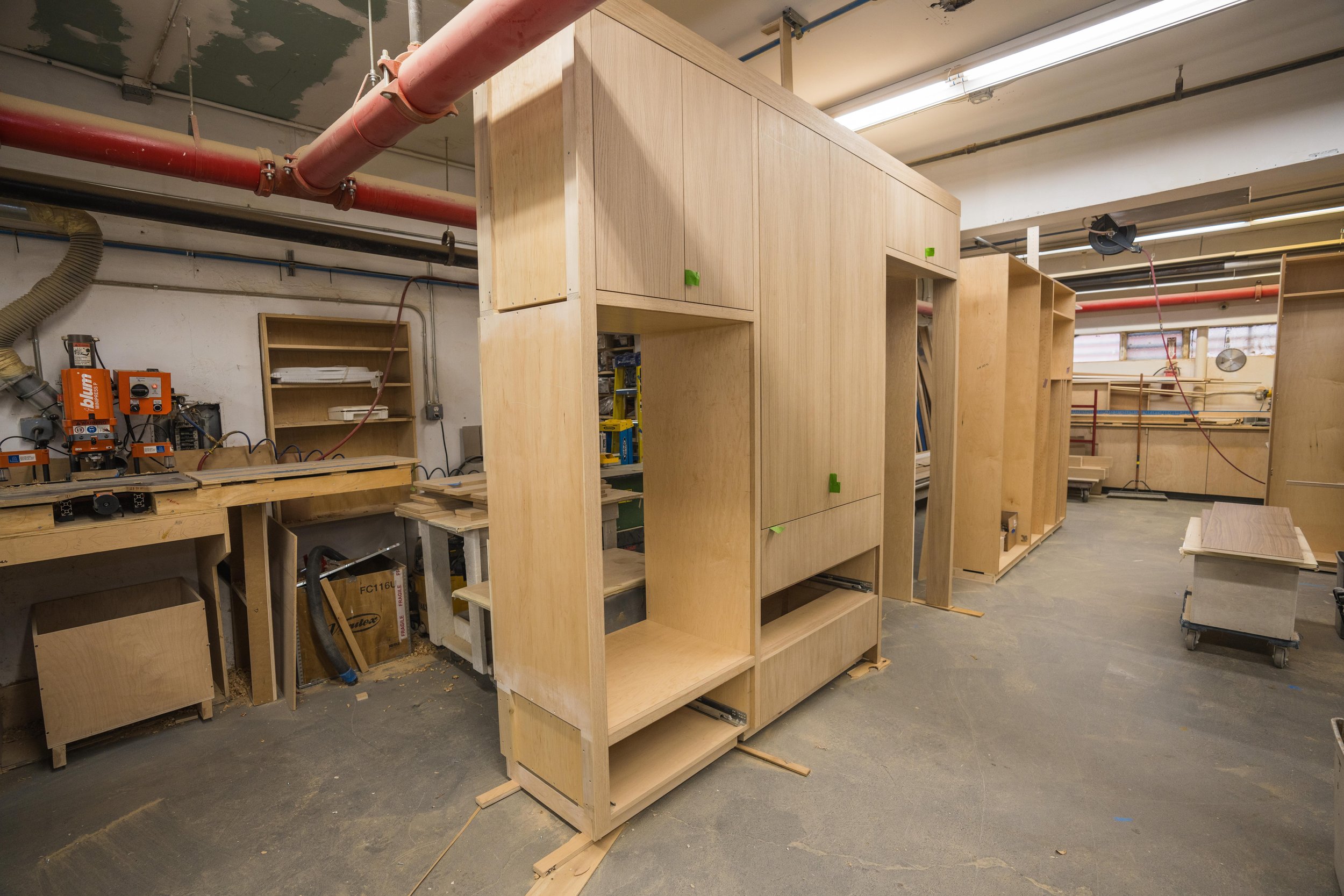 Wooden cabinet frame in a woodworking shop with tools and equipment in the background.