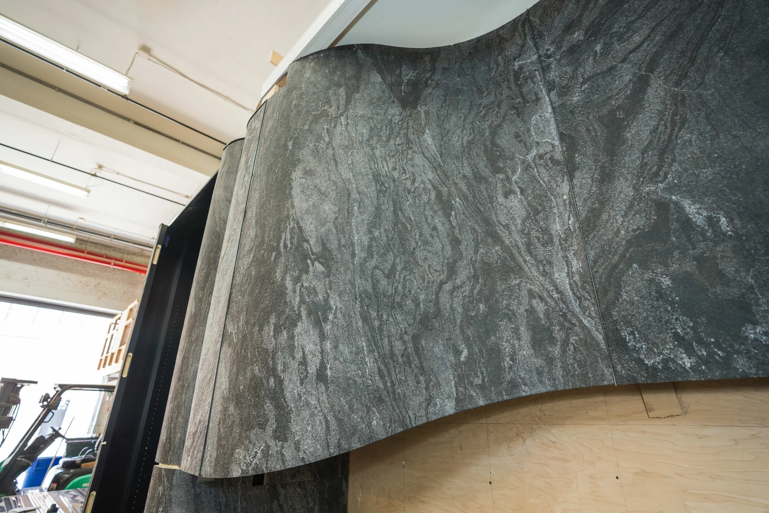 Close-up view of a dark grey stone countertop with a textured surface in an indoor setting, with part of a wooden floor visible at the bottom.