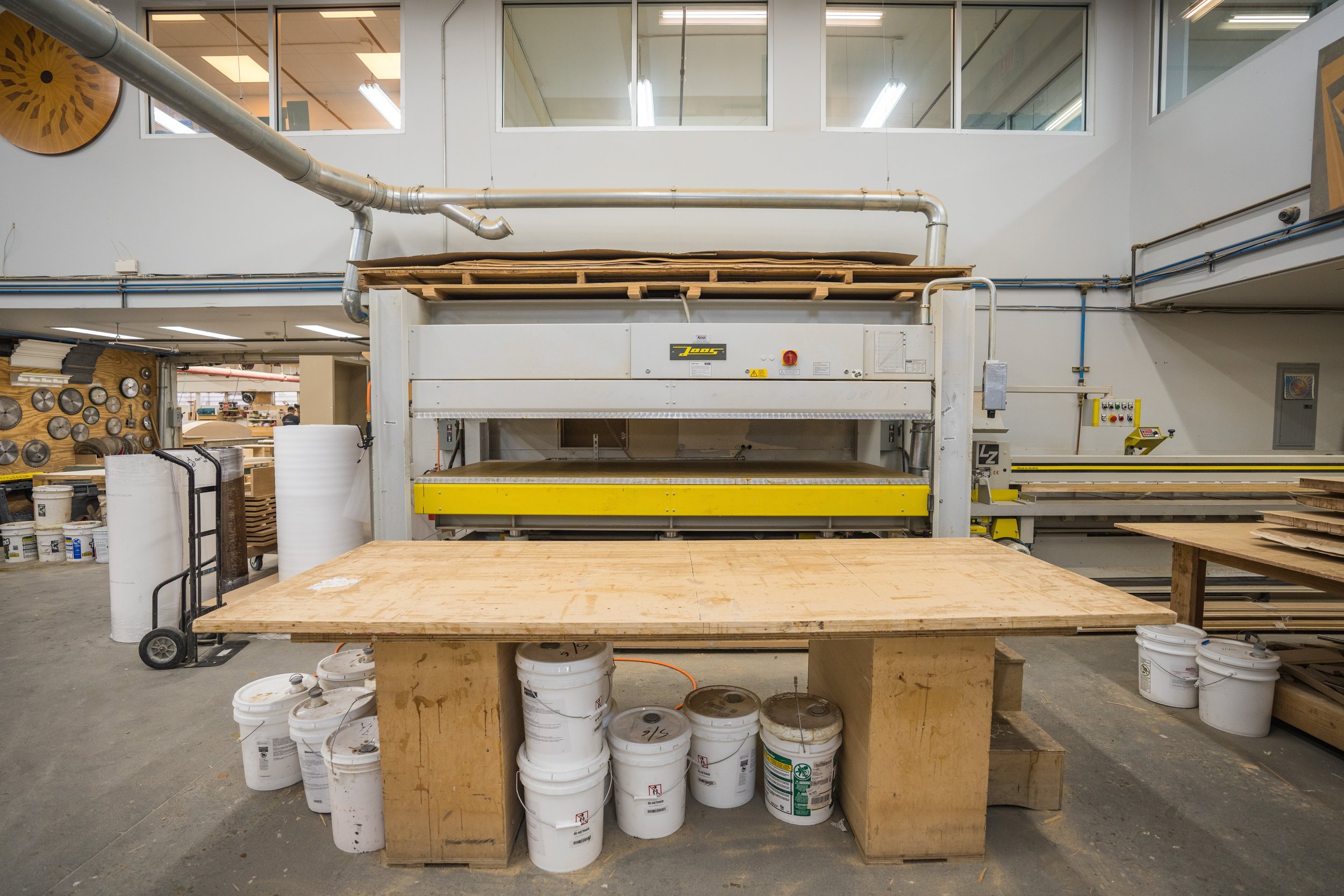 Woodworking shop with industrial machine, wooden work table, and buckets of paint or glue.