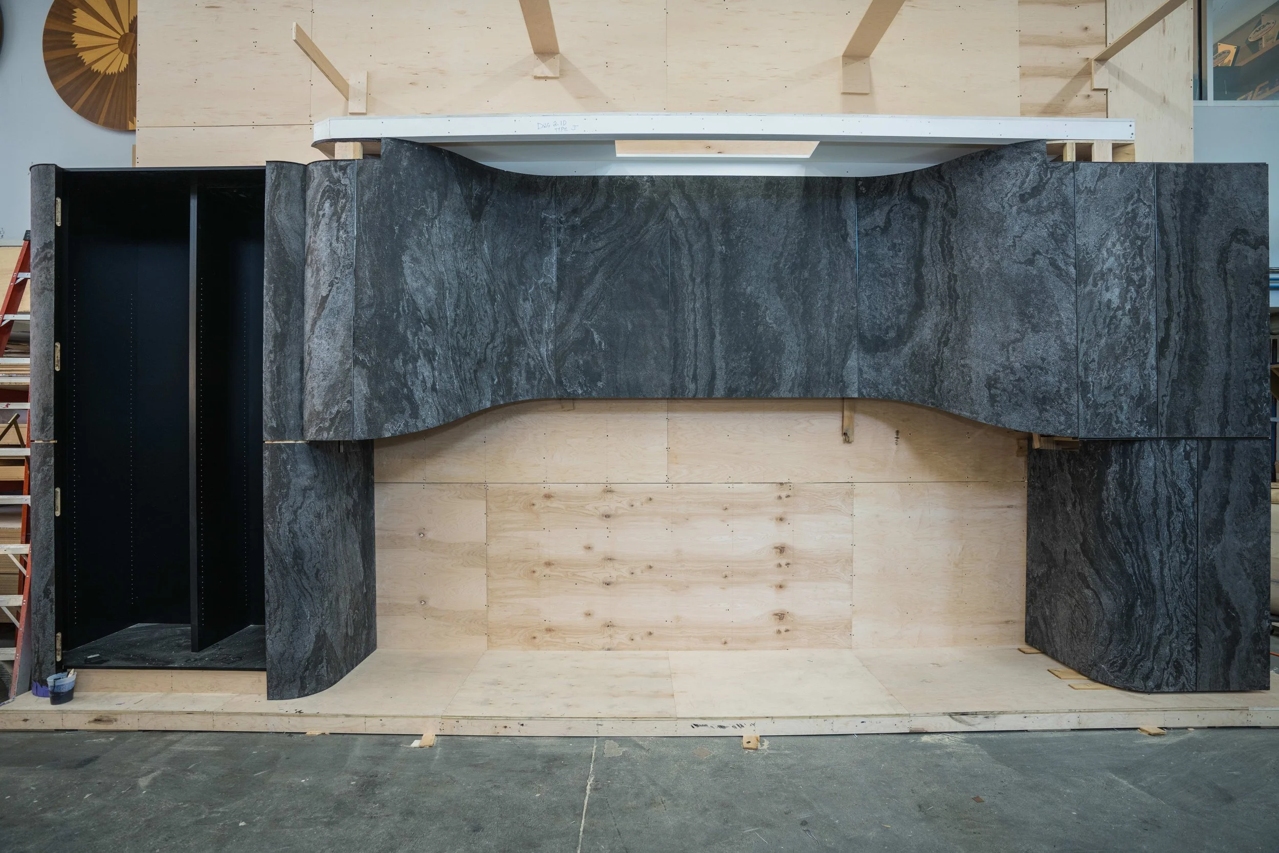 Large black and gray marble-like structure on a wooden platform in a workshop, with wooden panels and tools in the background.