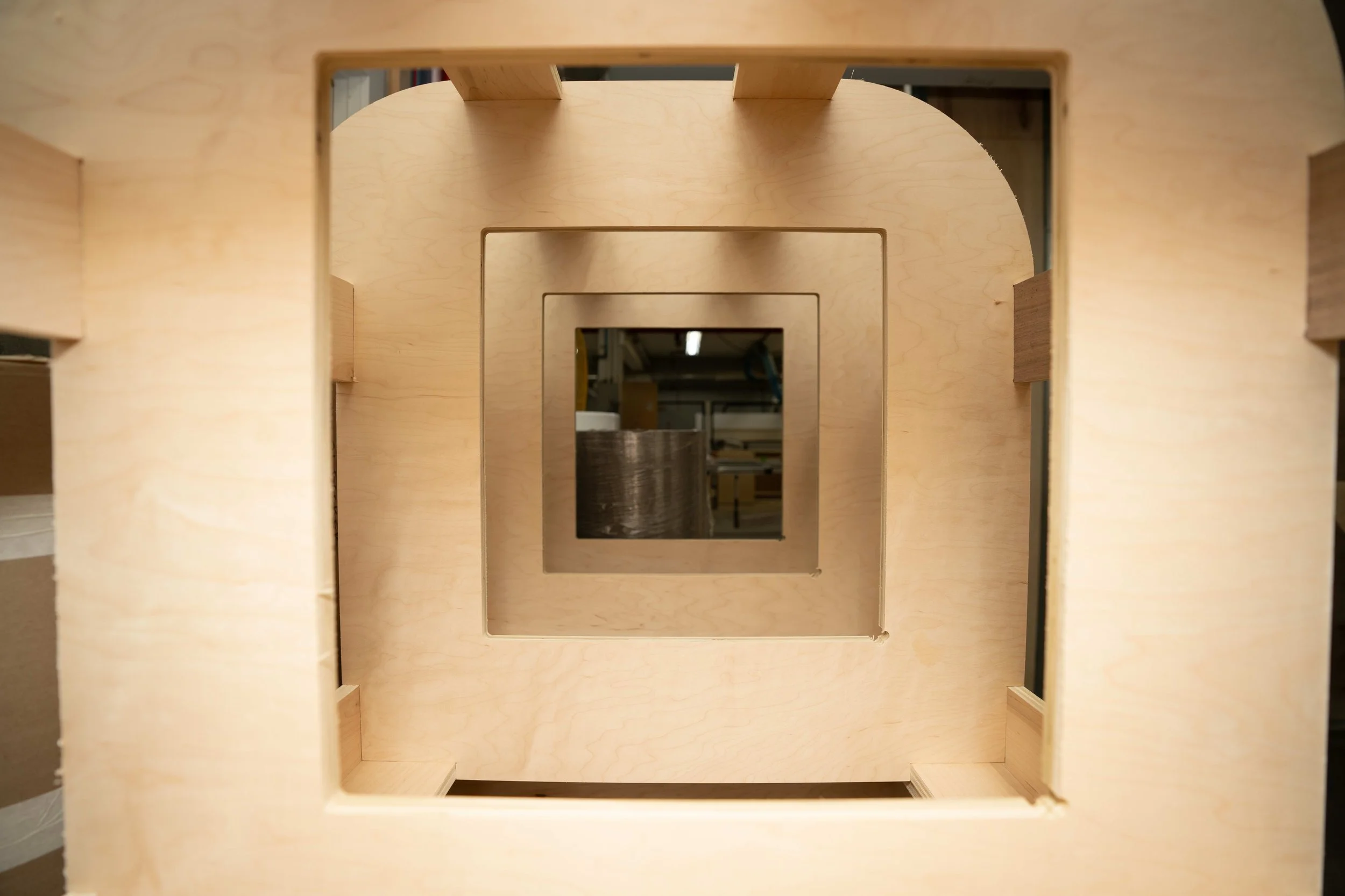 Multiple nested square cutouts in a wooden structure, creating a tunnel-like perspective.