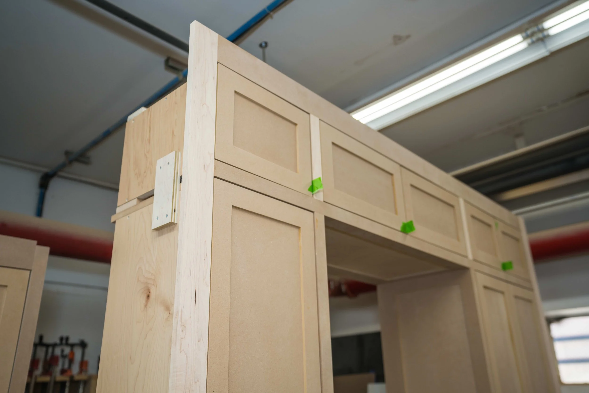 Wooden furniture pieces under construction, with visible screws and green tape, in a workshop.