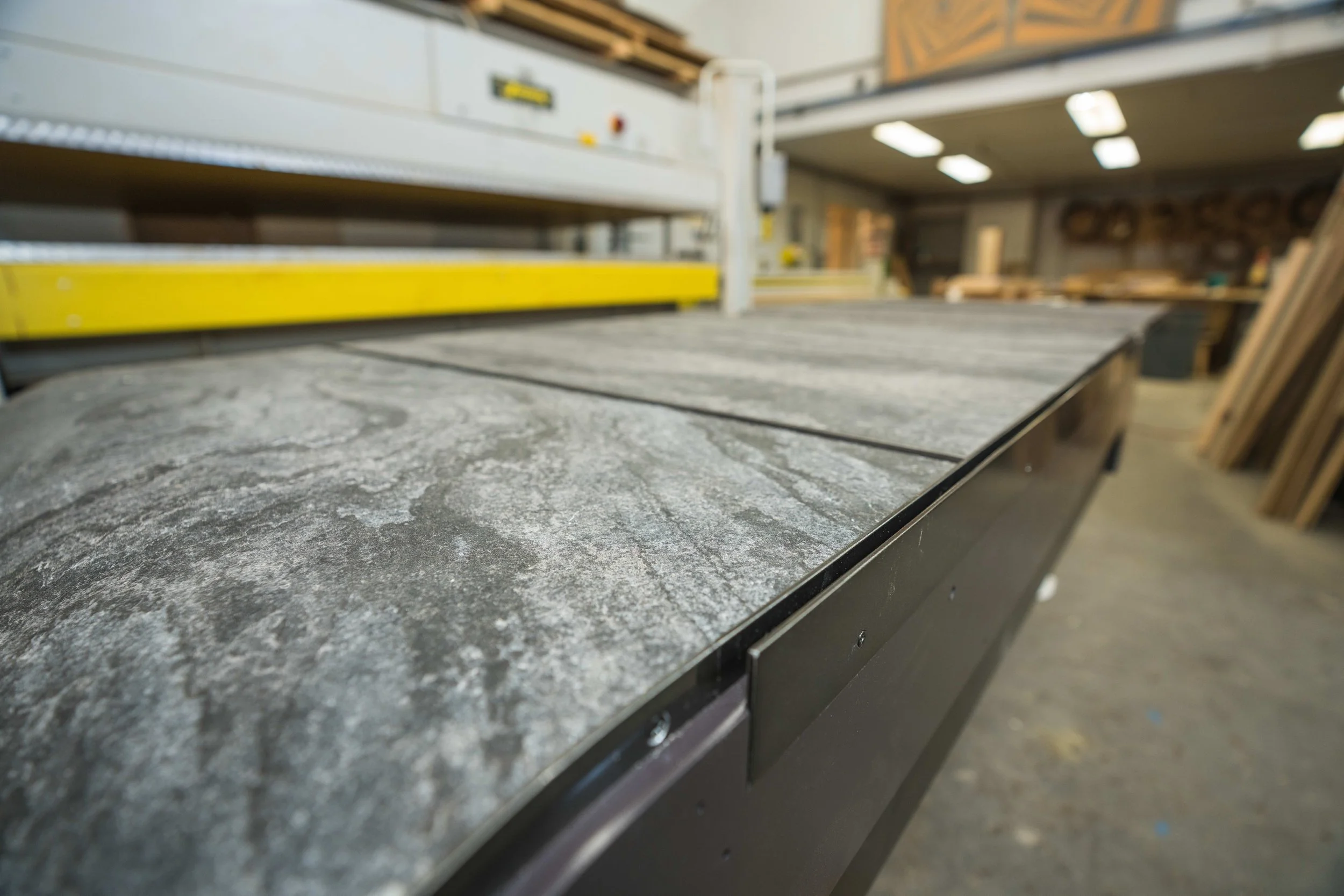 Close-up of a granite countertop in a woodworking shop with workshop equipment and shelves in the background.