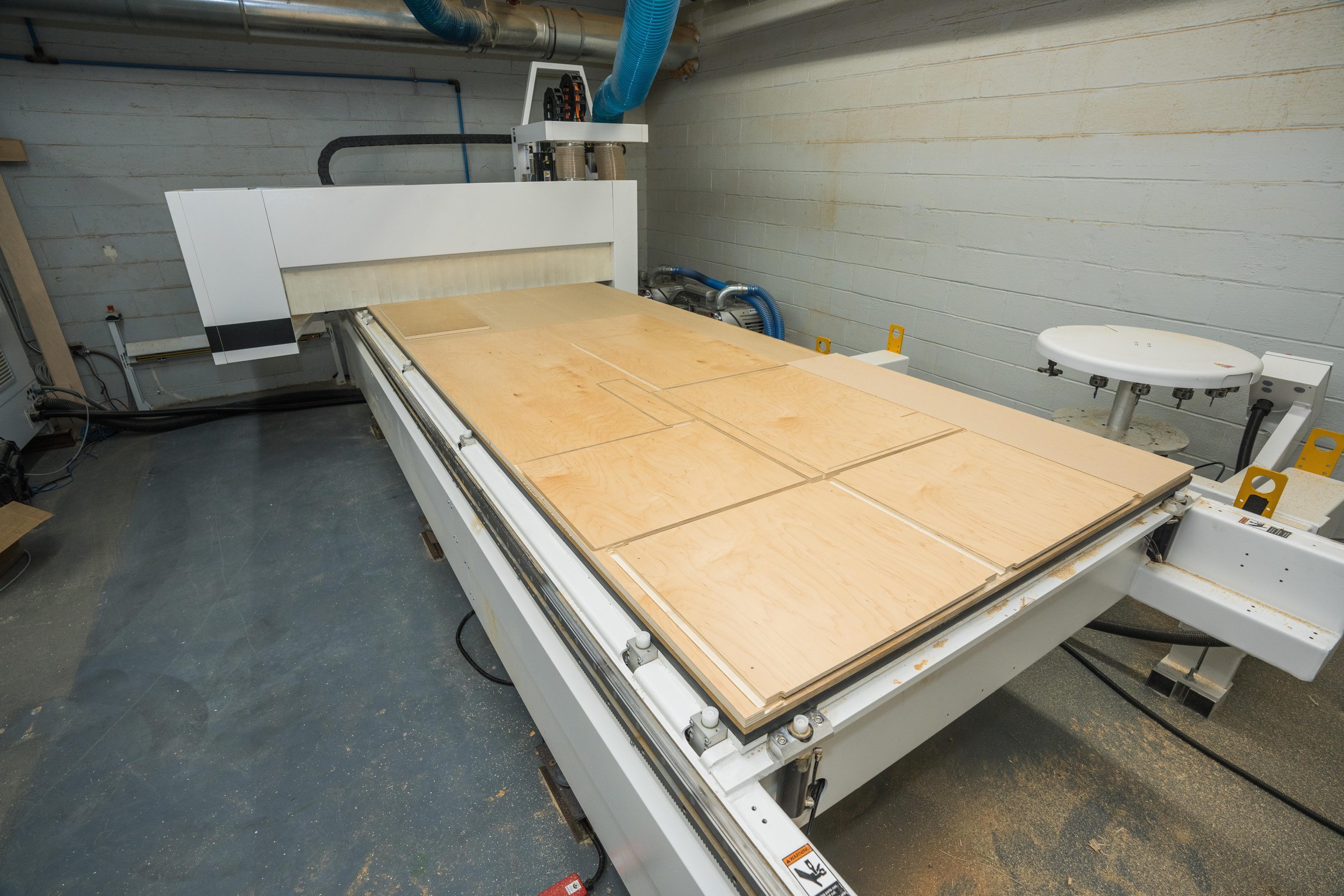 A CNC machine in a workshop cutting plywood sheets into shapes.