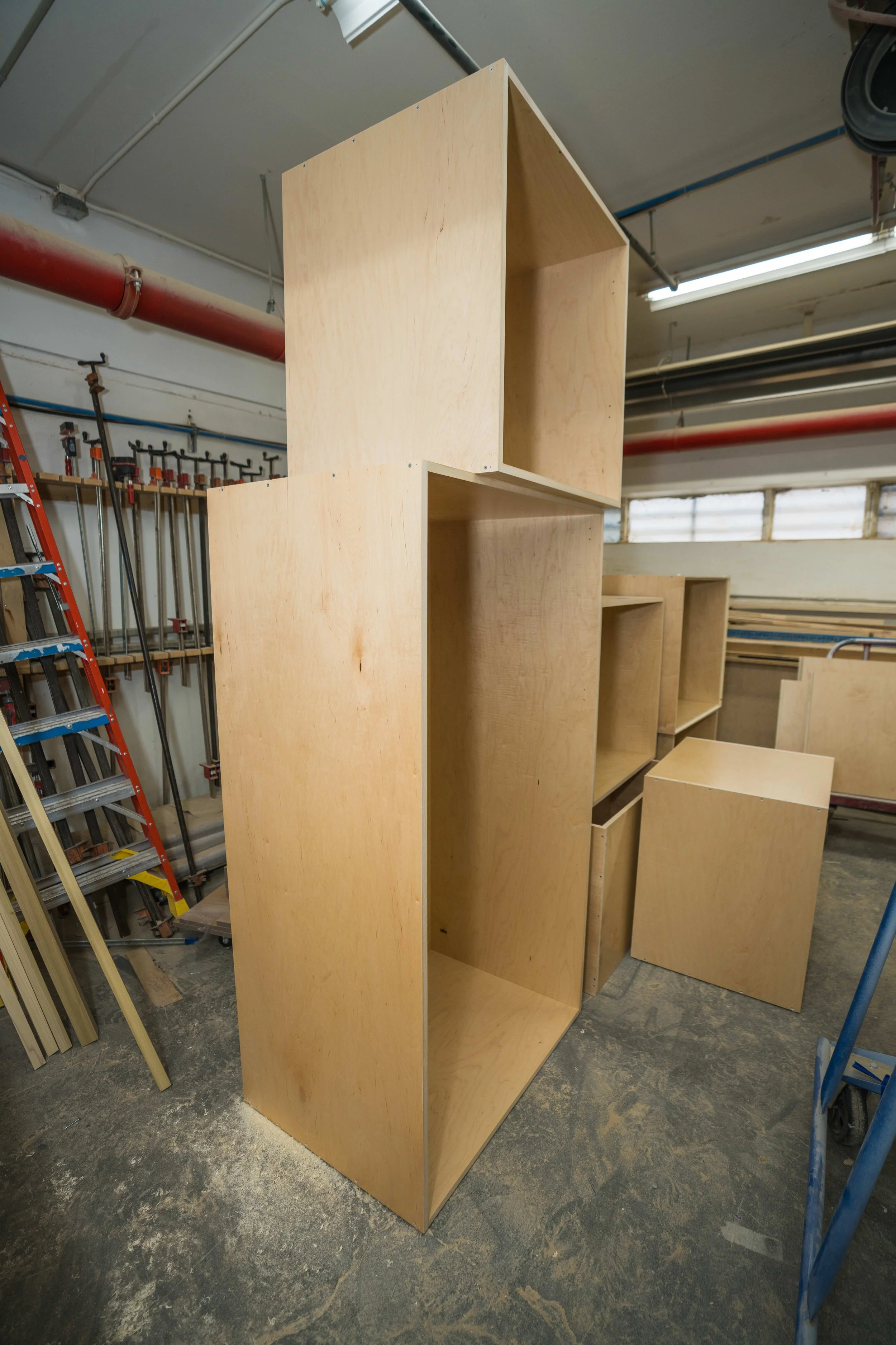Wooden shelving units in a woodworking shop, with tools and lumber in the background.