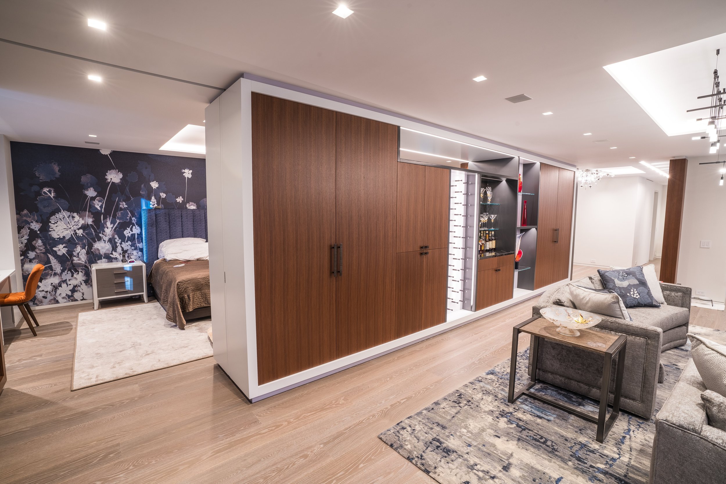 Modern open-concept living space with a bedroom, a wood-paneled wall with built-in shelving, and a sitting area with a sofa and coffee table.