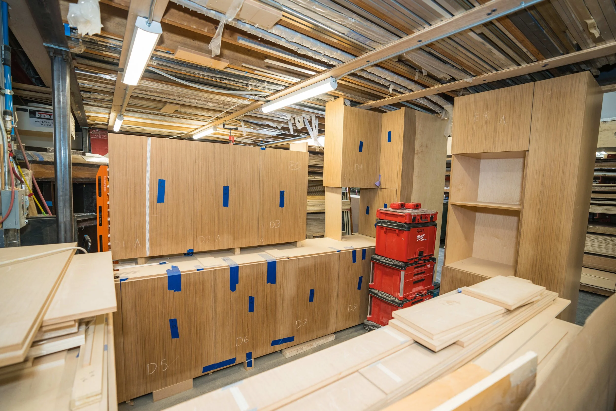 Wooden shelves and cabinets in a warehouse or workshop, with unfinished plywood and construction tools visible.