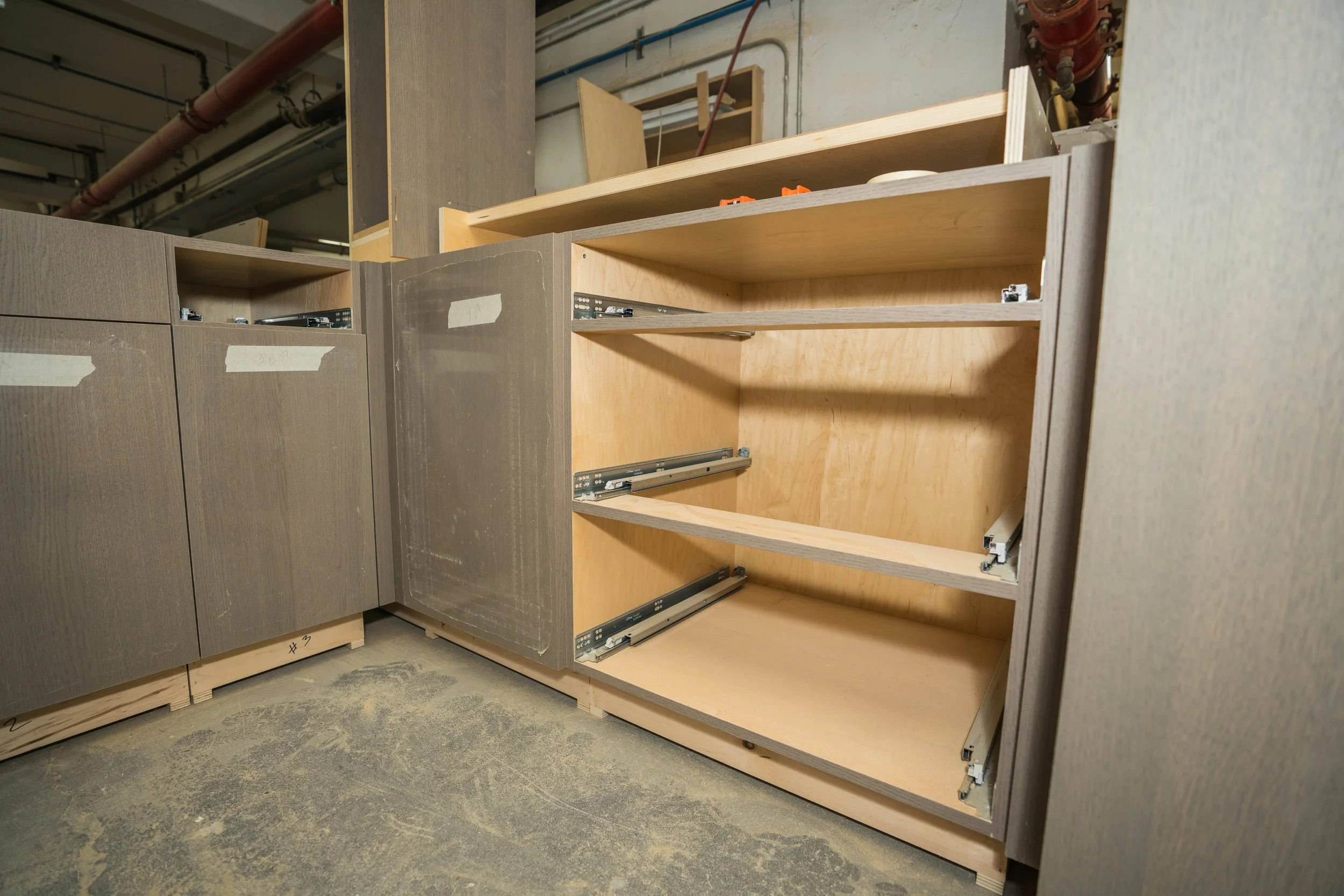 Unfinished wooden cabinets with metal drawer slides in a workshop or construction site.