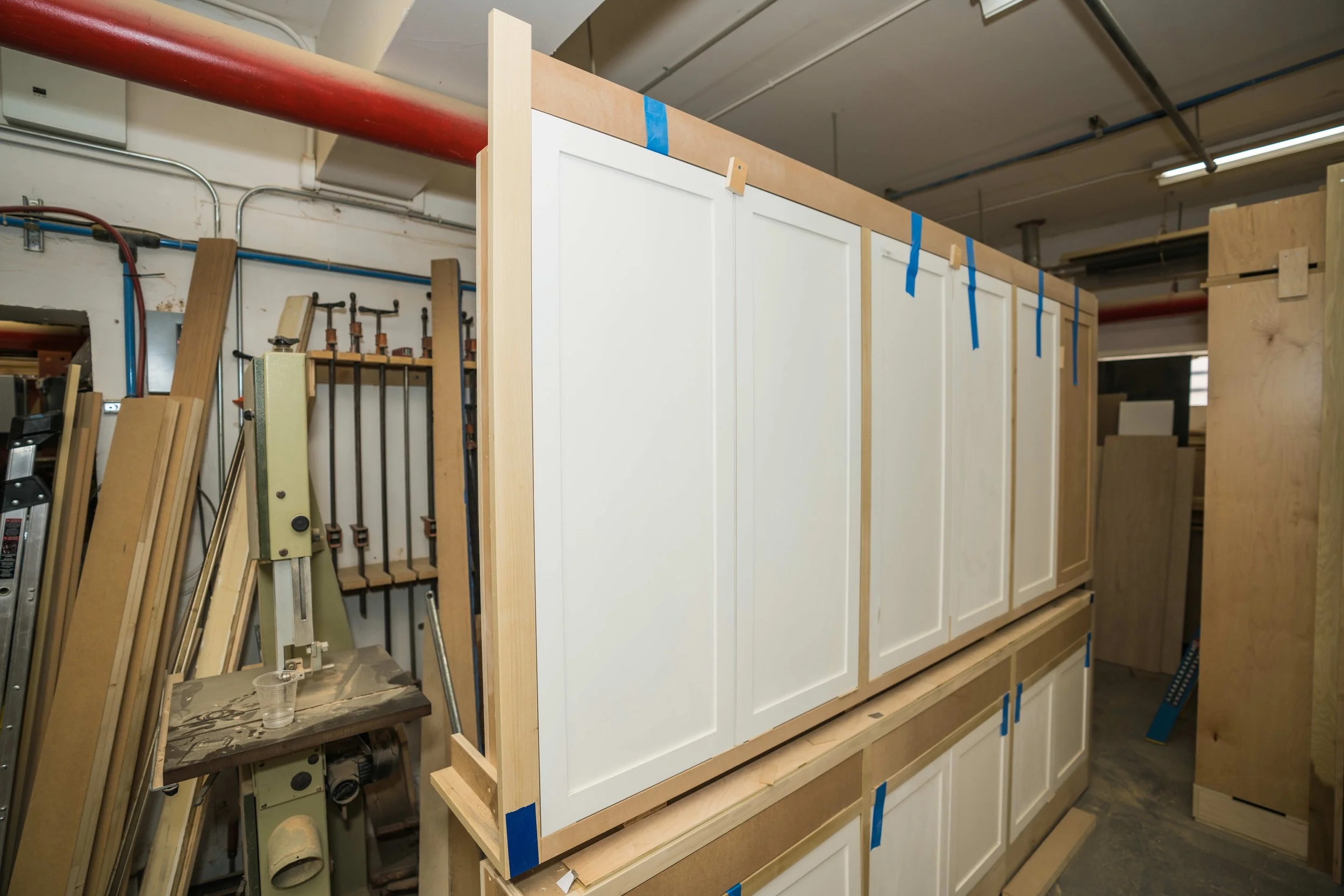 Workshop with a partially assembled kitchen cabinet, woodworking tools, and materials for cabinet construction.