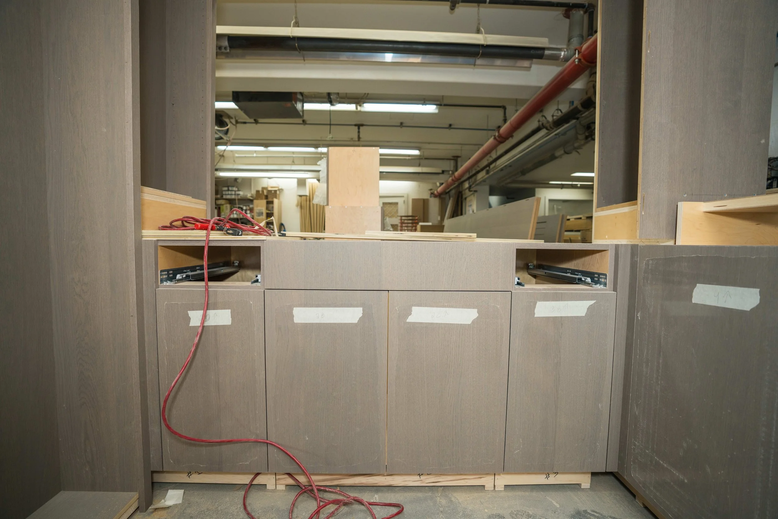 Wooden cabinetry under construction with visible electrical wiring and hardware, in a woodworking workshop.