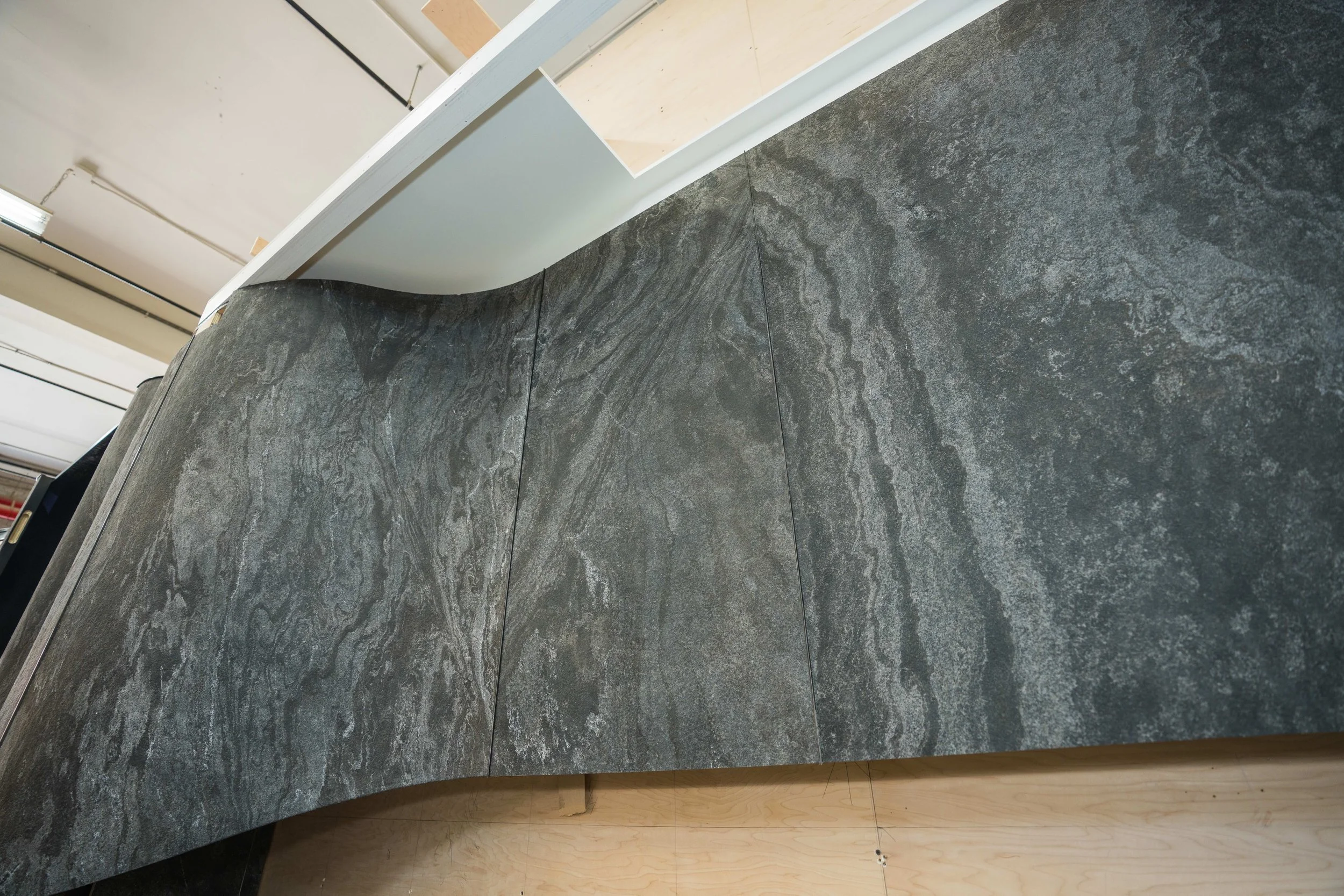 Close-up of a dark gray stone wall with natural veining and texture, with a section of lighter wood floor visible at the bottom.