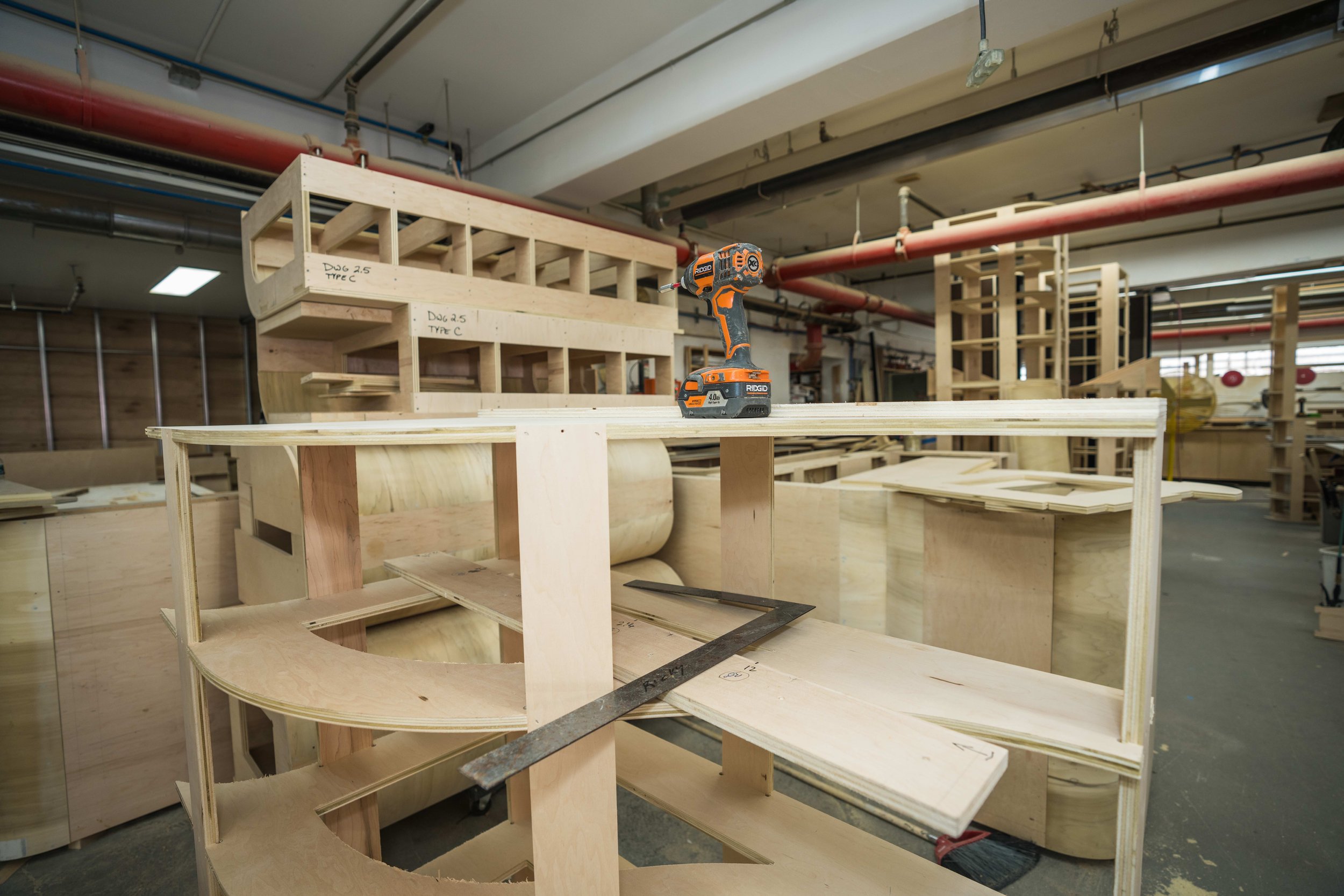 Interior of a woodworking workshop with wooden structures, a cordless drill, and various tools and materials for building furniture or projects.