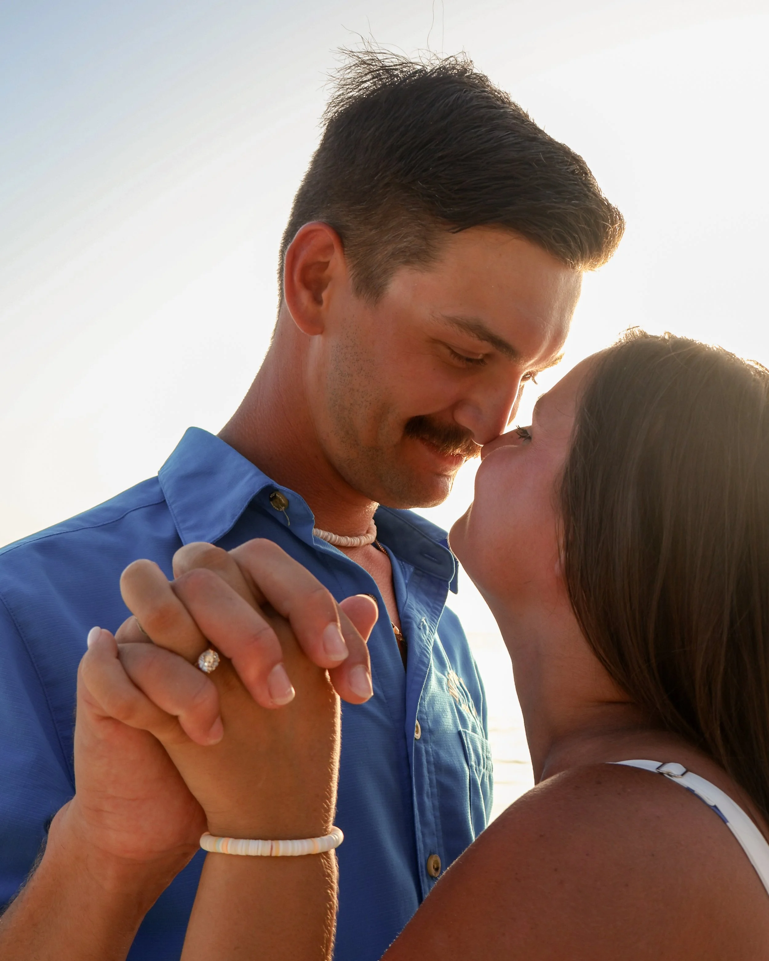 A couple sharing a romantic moment, with the man holding the woman's hand and both close to each other, outdoors with clear lighting.