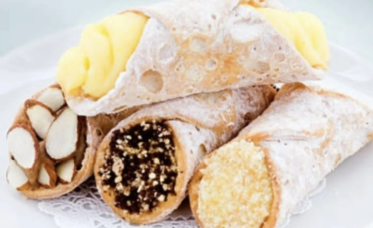 An assortment of five cannoli on a white doily-lined plate, showcasing different fillings and toppings.