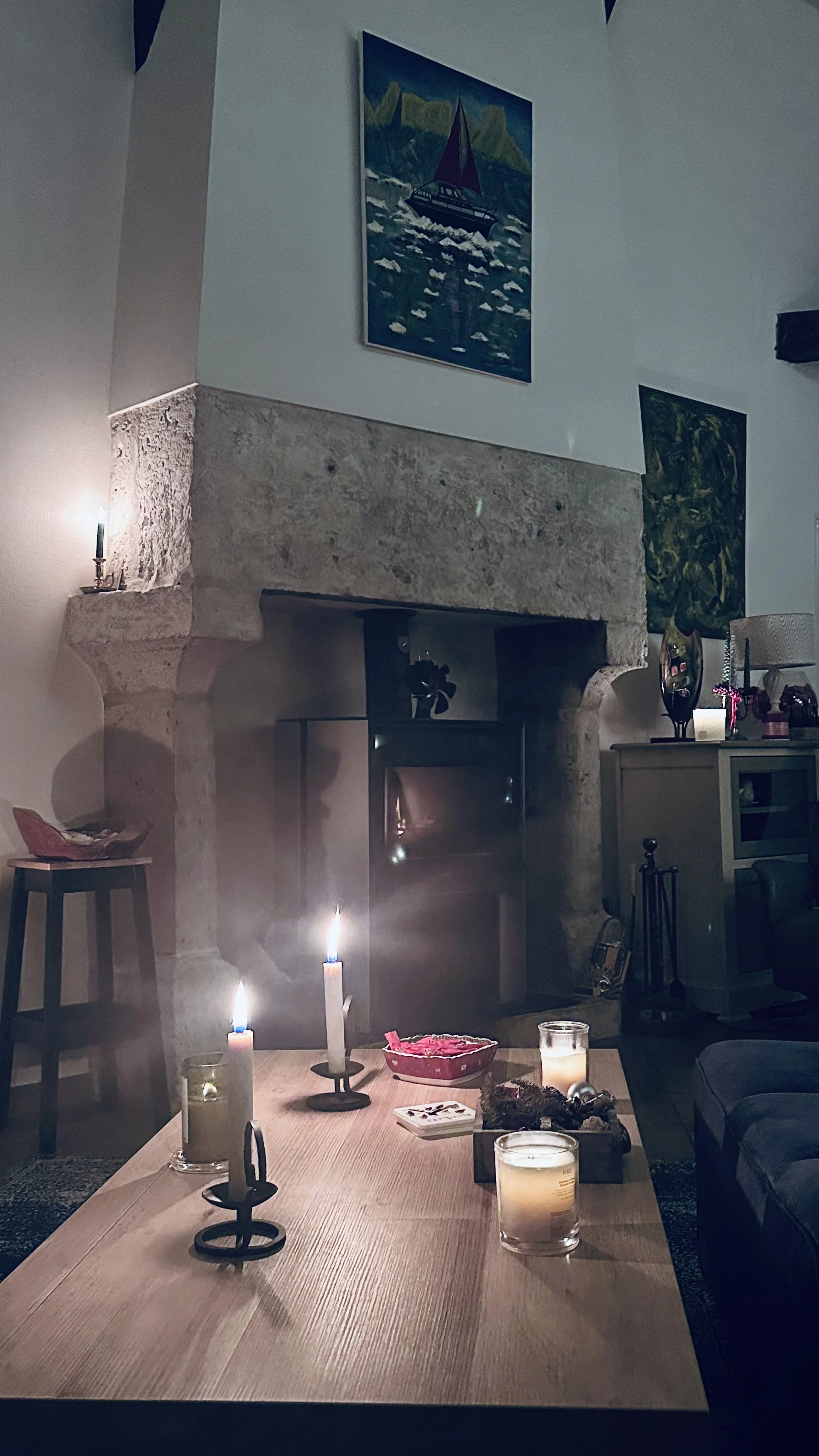 Living room with lit candles on a coffee table, a stone fireplace, and artwork on the walls.
