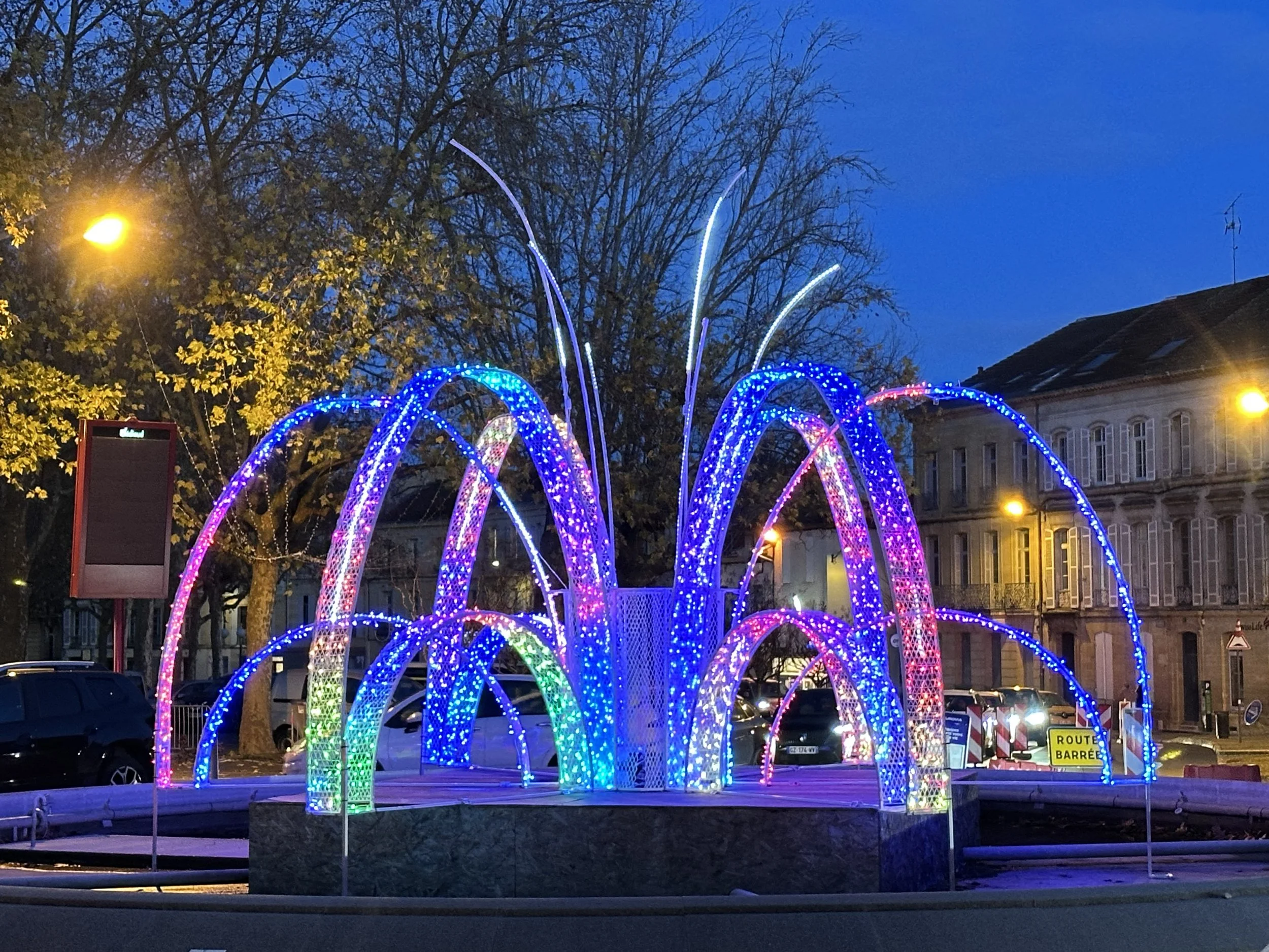 Colorful illuminated fountain with arcs of blue, pink, and green lights in Bergerac at Christmas.