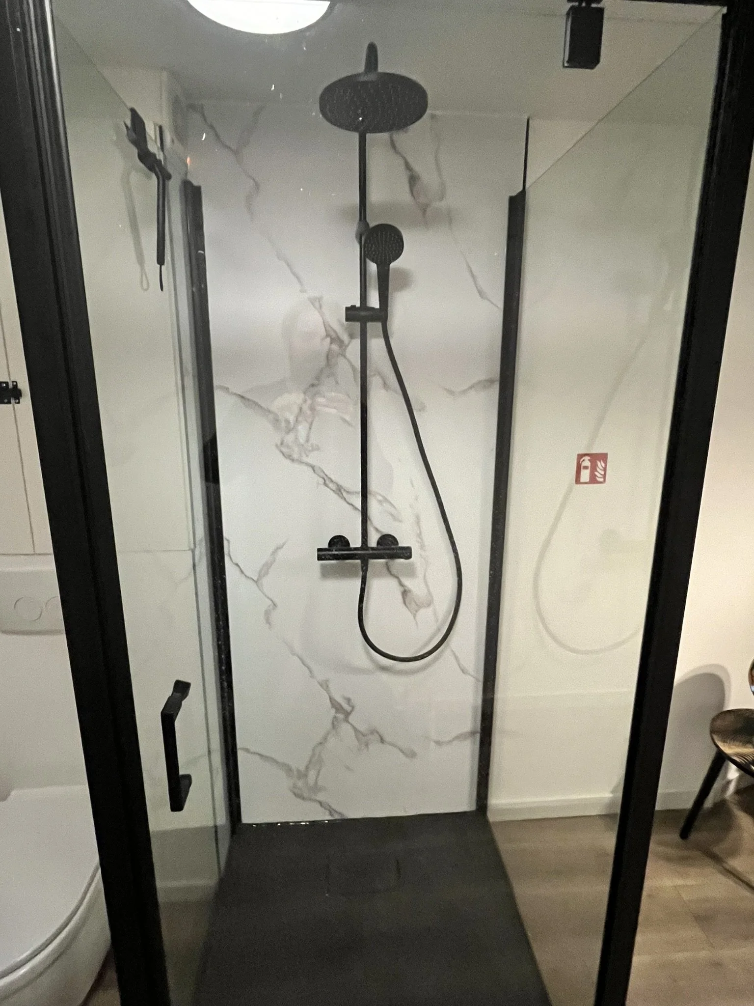 Inloopdouche met zwarte handdouche en waterkraan, omgeven door een glazen deur met zwarte handgrepen, met een marmeren patroon op de muur.