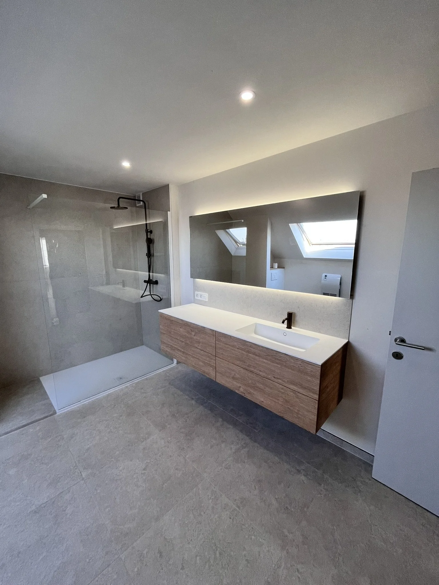 Moderne badkamer met een inloopdouche, wastafel met grote spiegel, en twee dakramen voor natuurlijk licht.