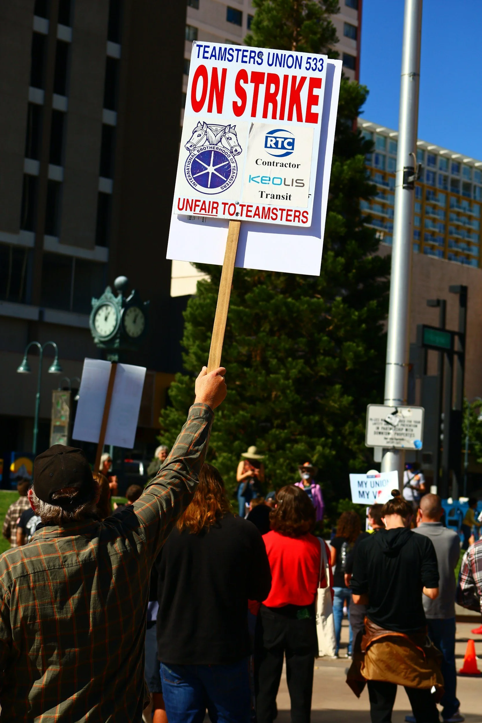 Protester holding a sign that reads 'ON STRIKE' during a protests or demonstration, with a crowd in the background.
