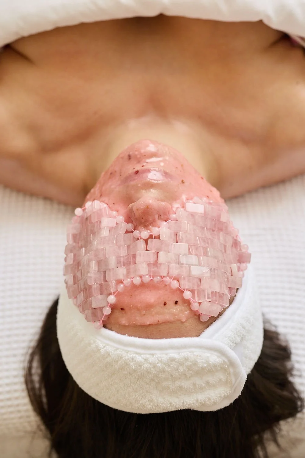 A person lying down with a pink, textured nose surrounded by pink beads, covered with a white towel or cloth, in a medical or spa setting.