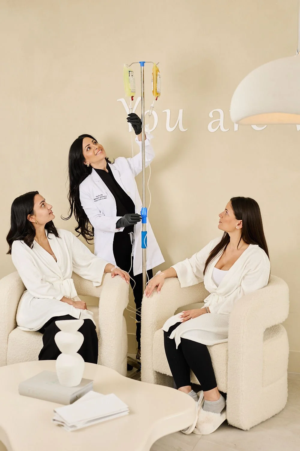 Medical professional setting up an IV drip for two seated women in a waiting room.