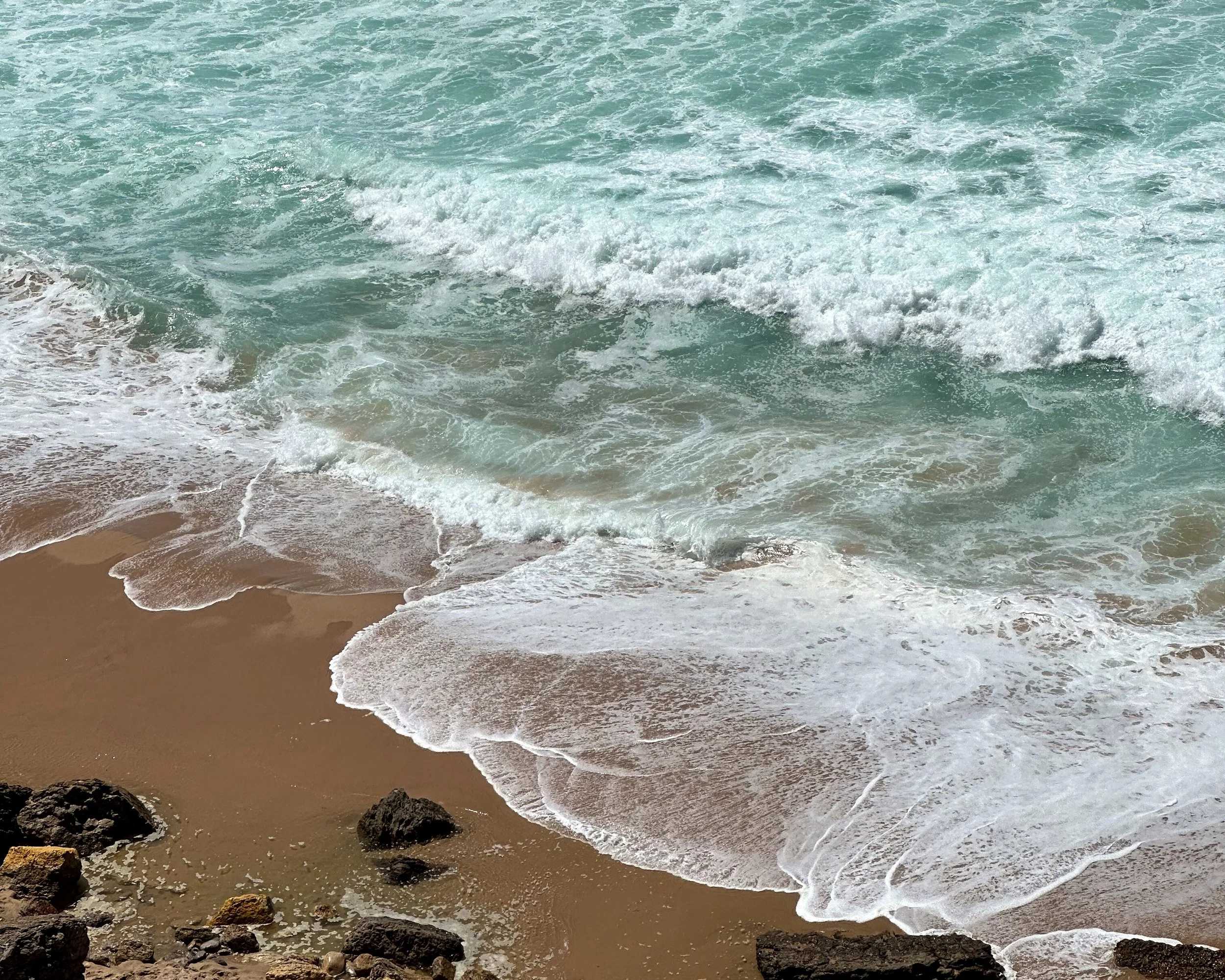 Waves crashing onto sandy beach with rocks in foreground.