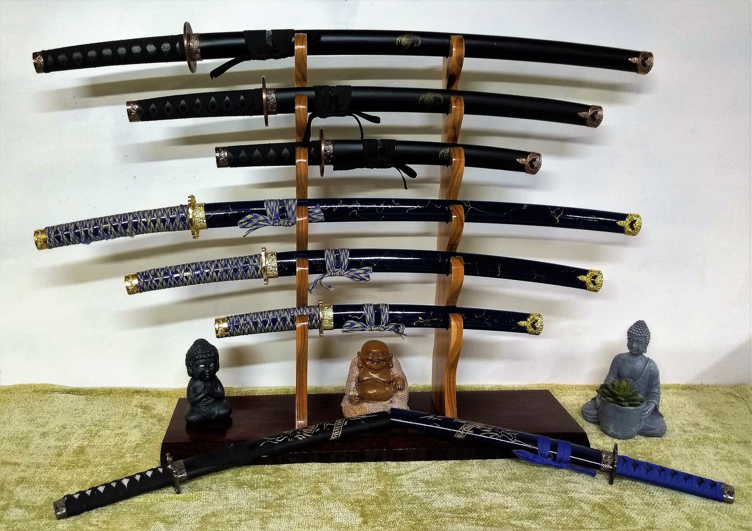 An assortment of Japanese swords on a wooden display rack with small Buddha statues and a green cloth underneath.