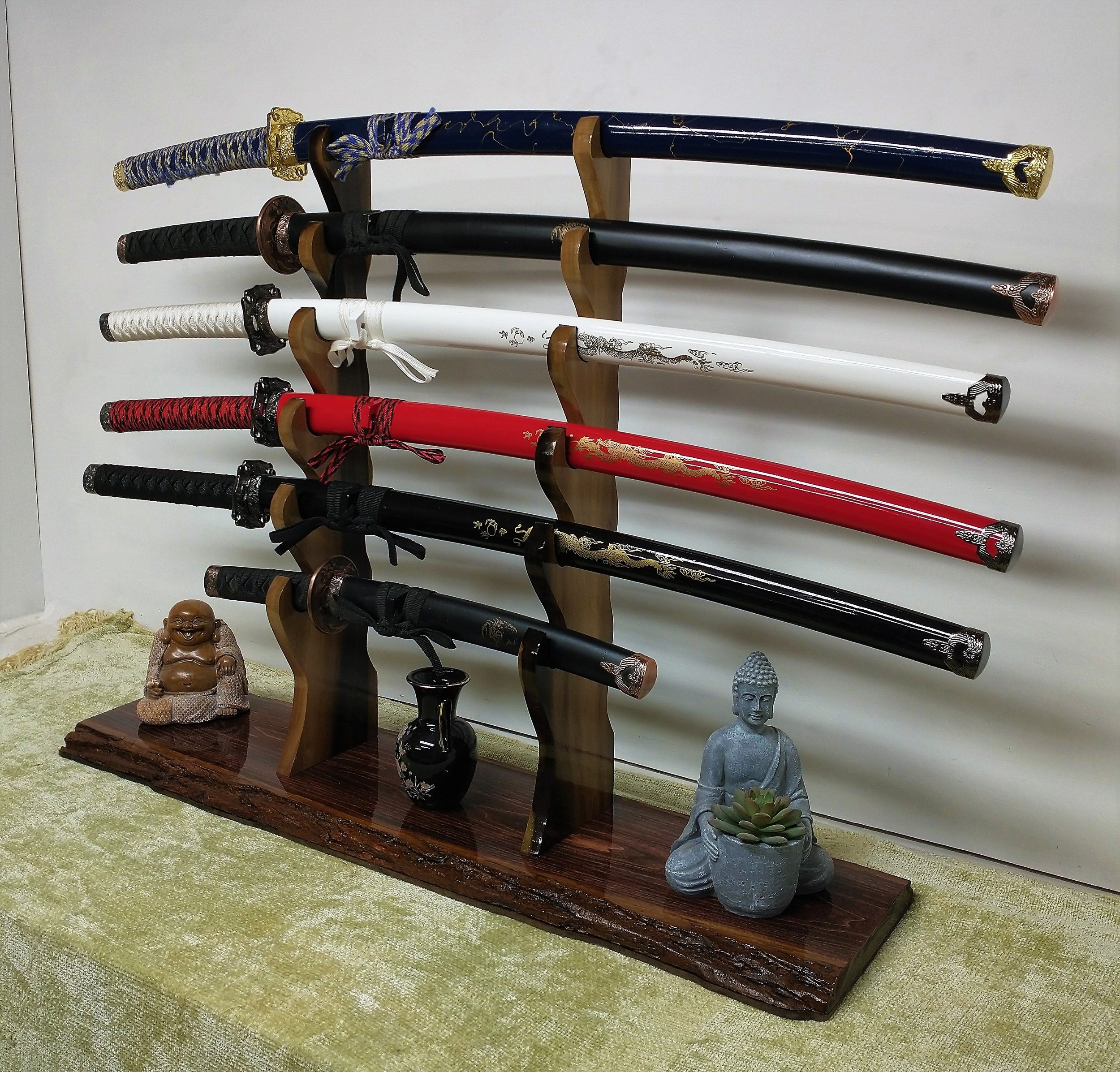 Display of seven decorative swords on wooden racks, with Buddhist statues and a small black vase on a wooden base, on a green tablecloth.