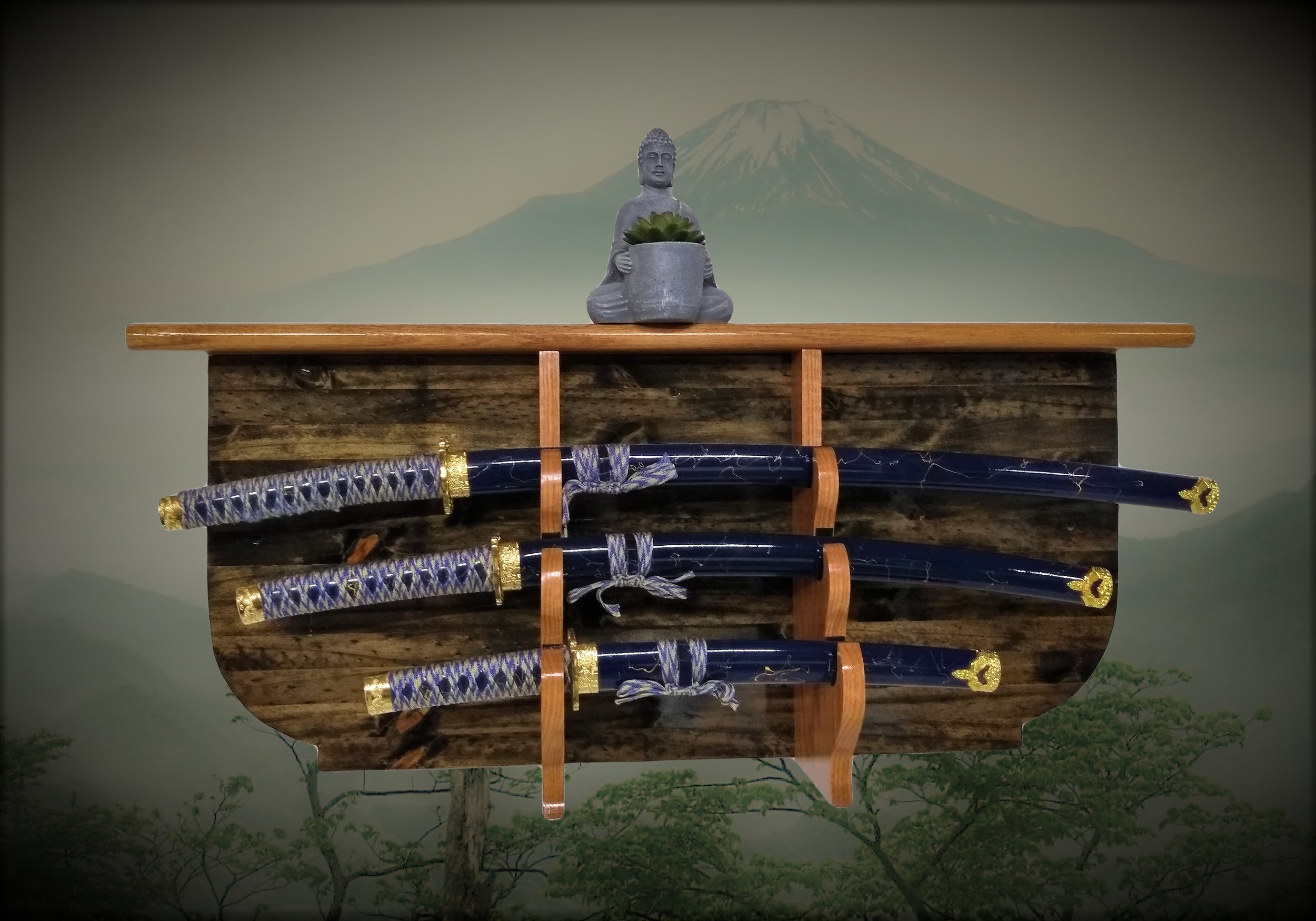 Display of three Japanese swords with decorative handles on a wooden stand, a small Buddha statue holding a potted succulent on top, and Mount Fuji in the background mural.