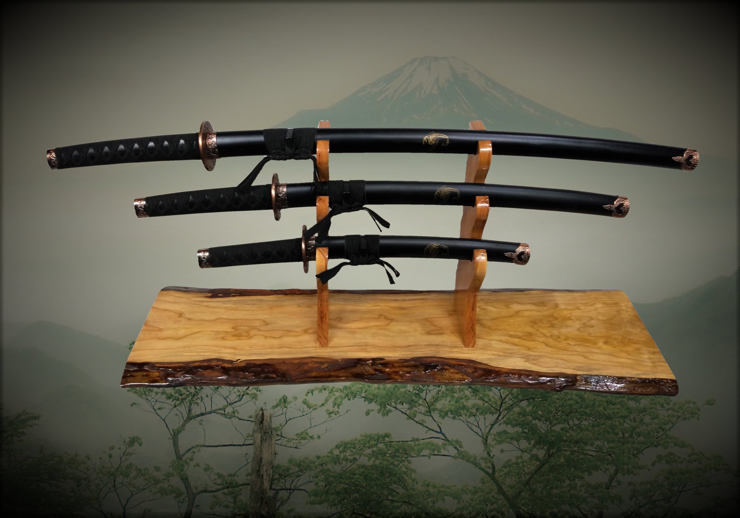 Three Japanese-style swords with black handles and copper accents mounted on a wooden display stand against a background featuring a mountain and trees.