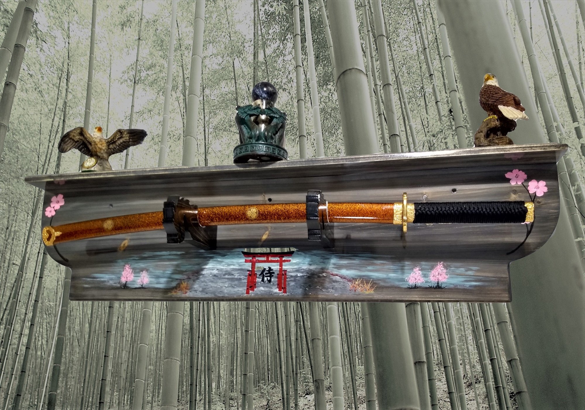 Decorative shelf with Japanese-themed ornaments in front of a bamboo forest background, featuring two eagle figurines, a samurai sword, and a Buddha sculpture.