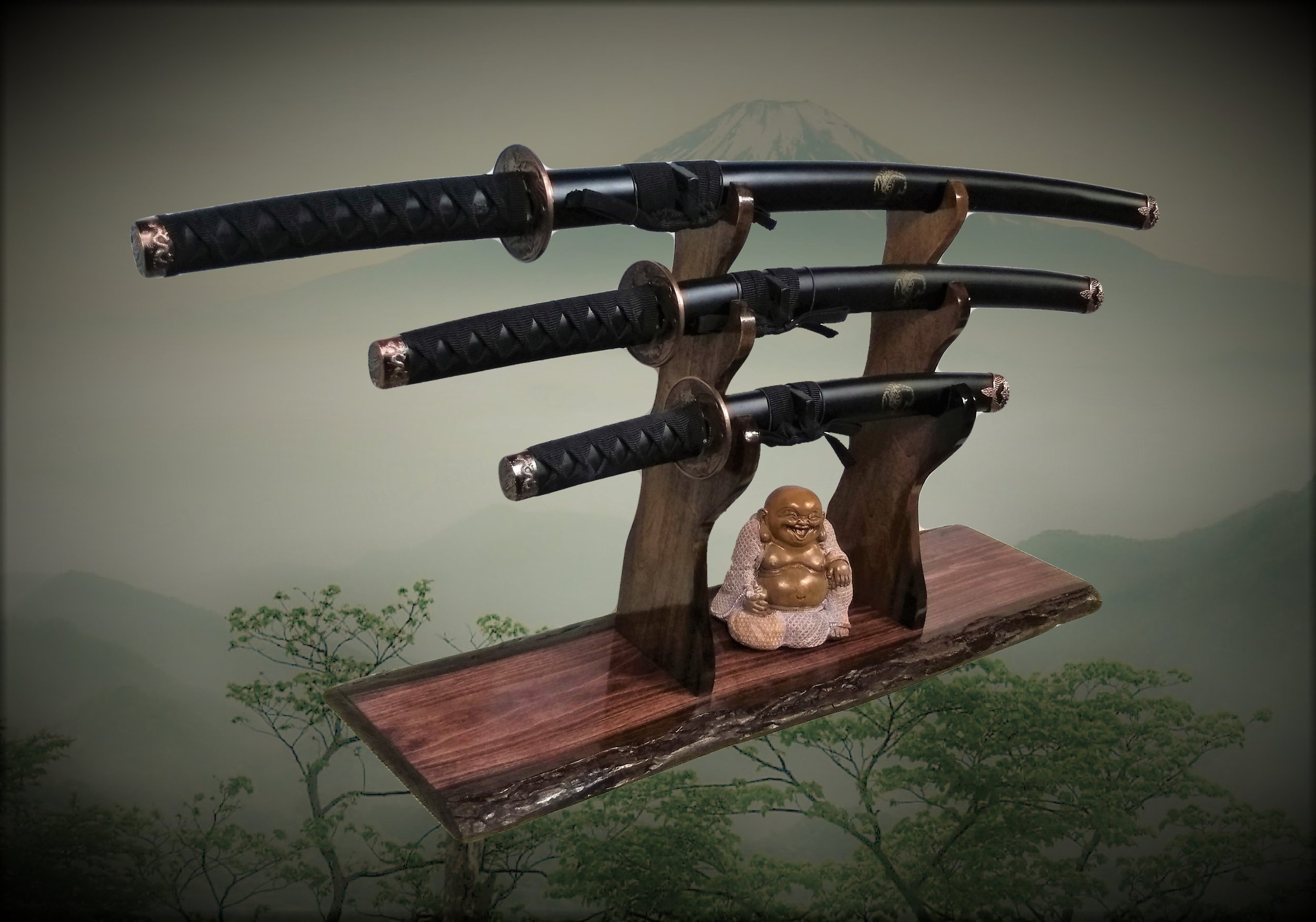 Three Japanese swords mounted on a wooden display stand with a small smiling Buddha figurine, with a mountain in the background.