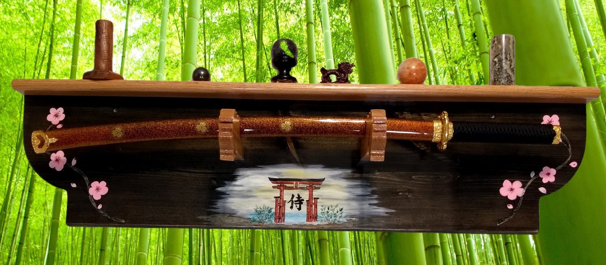 Decorative display with a katana sword, small carved statues, and painted Japanese symbols against a background of green bamboo stalks.