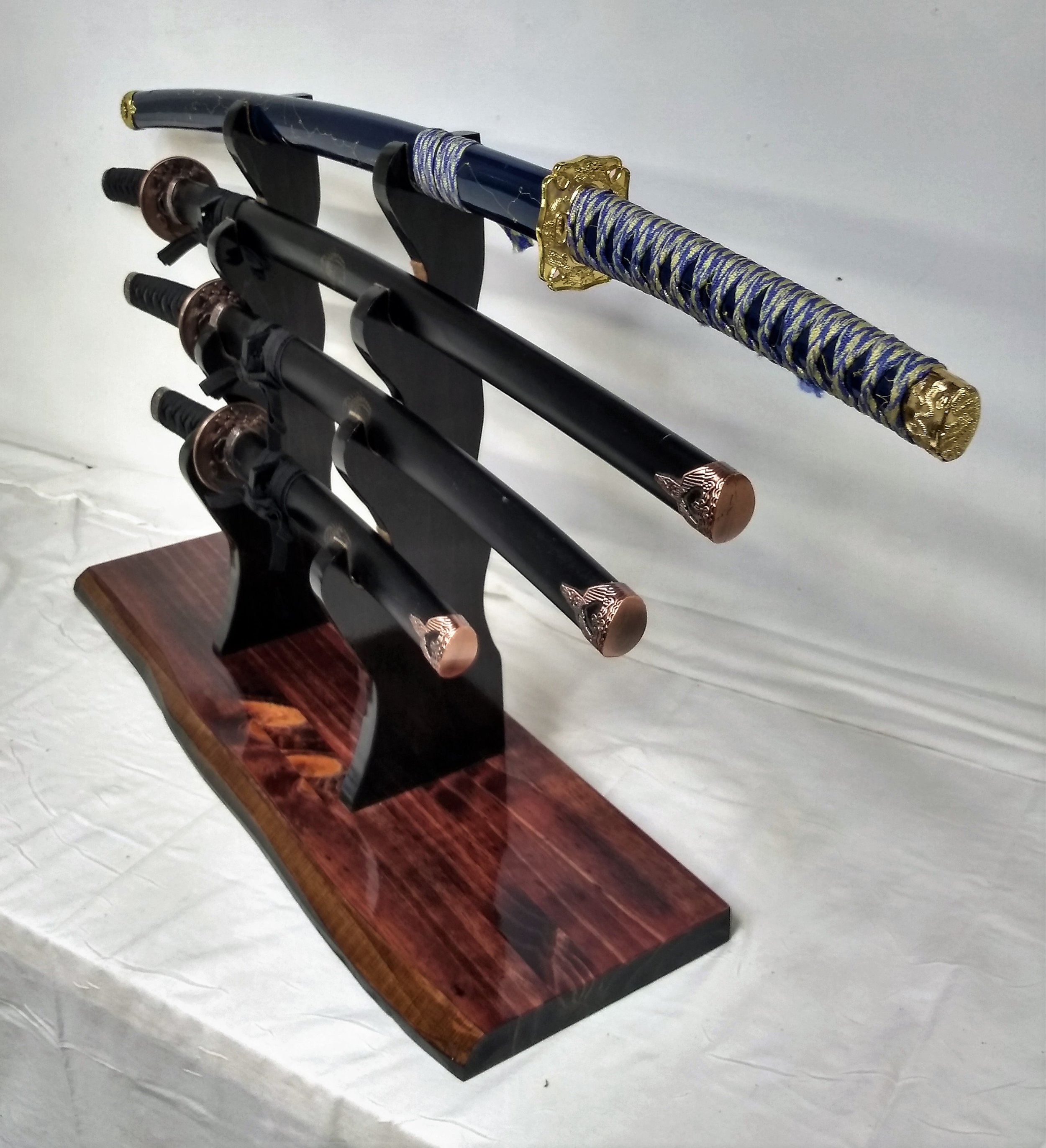 Display of three decorative Japanese swords with black and gold handles, mounted on a wooden stand.
