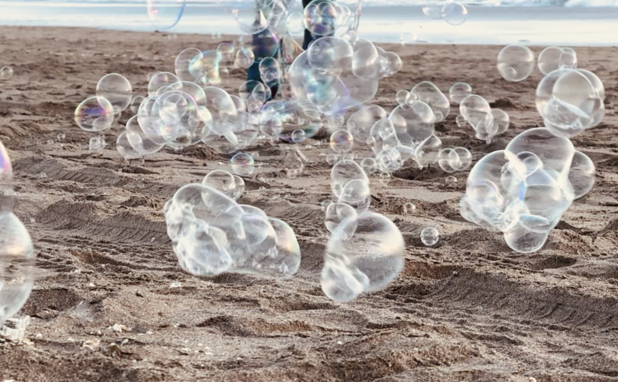 Bubbles floating above a sandy beach near the water.