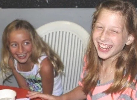 Two young girls smiling and laughing at a table.
