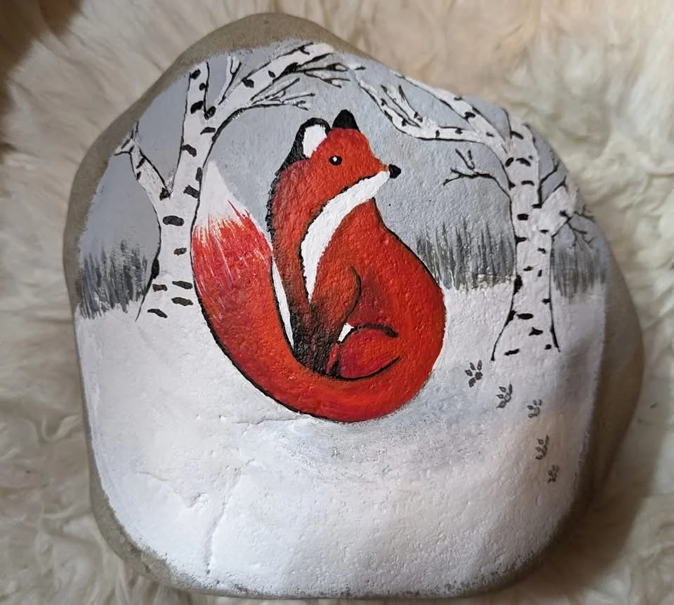 Painted design of a red fox sitting among trees on a rock with a snowy background.