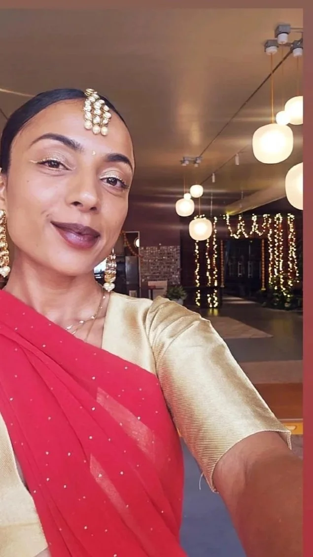 A woman dressed in traditional Indian attire taking a selfie indoors decorated with string lights and hanging lanterns.