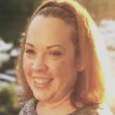 A woman smiling outdoors during sunset with water in the background.