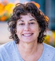A white woman with dark hair and hoop earrings smiling into the camera.